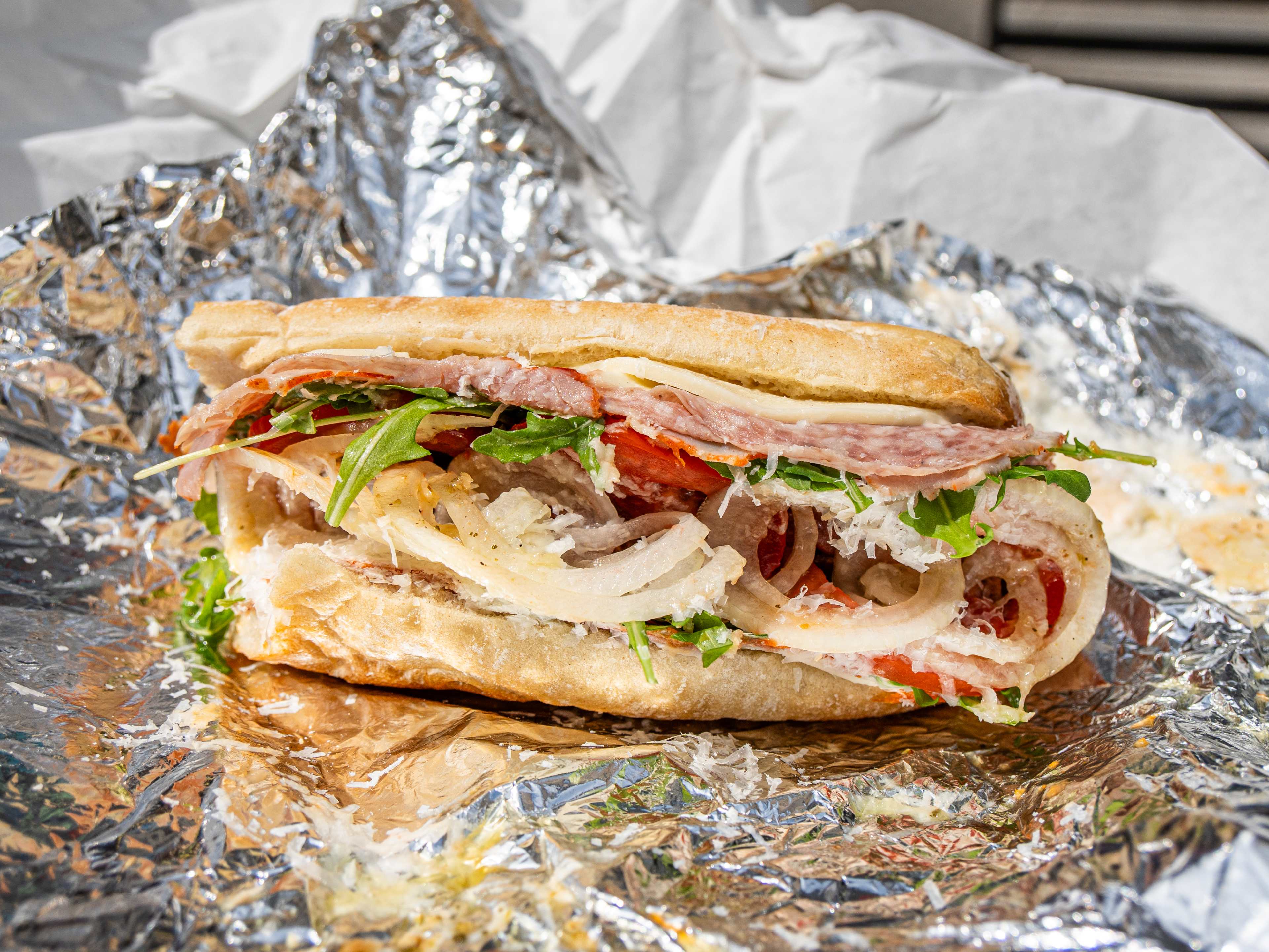 italian hoagie stuffed with meat, cheese, and veggies on tin foil wrapper