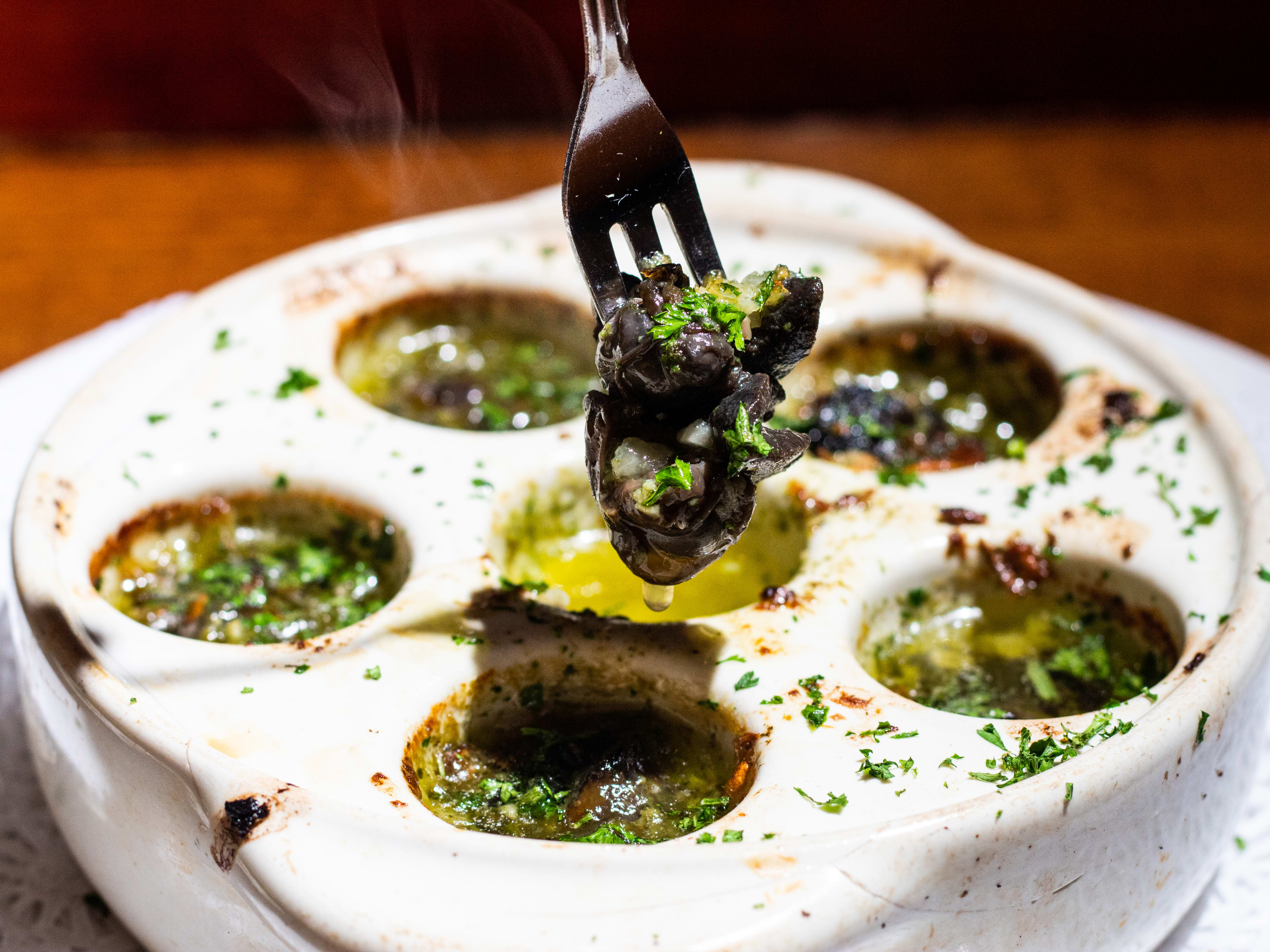 a staud filled with escargots, garlic, a nd parsley. There is a small fork holding an escargot.