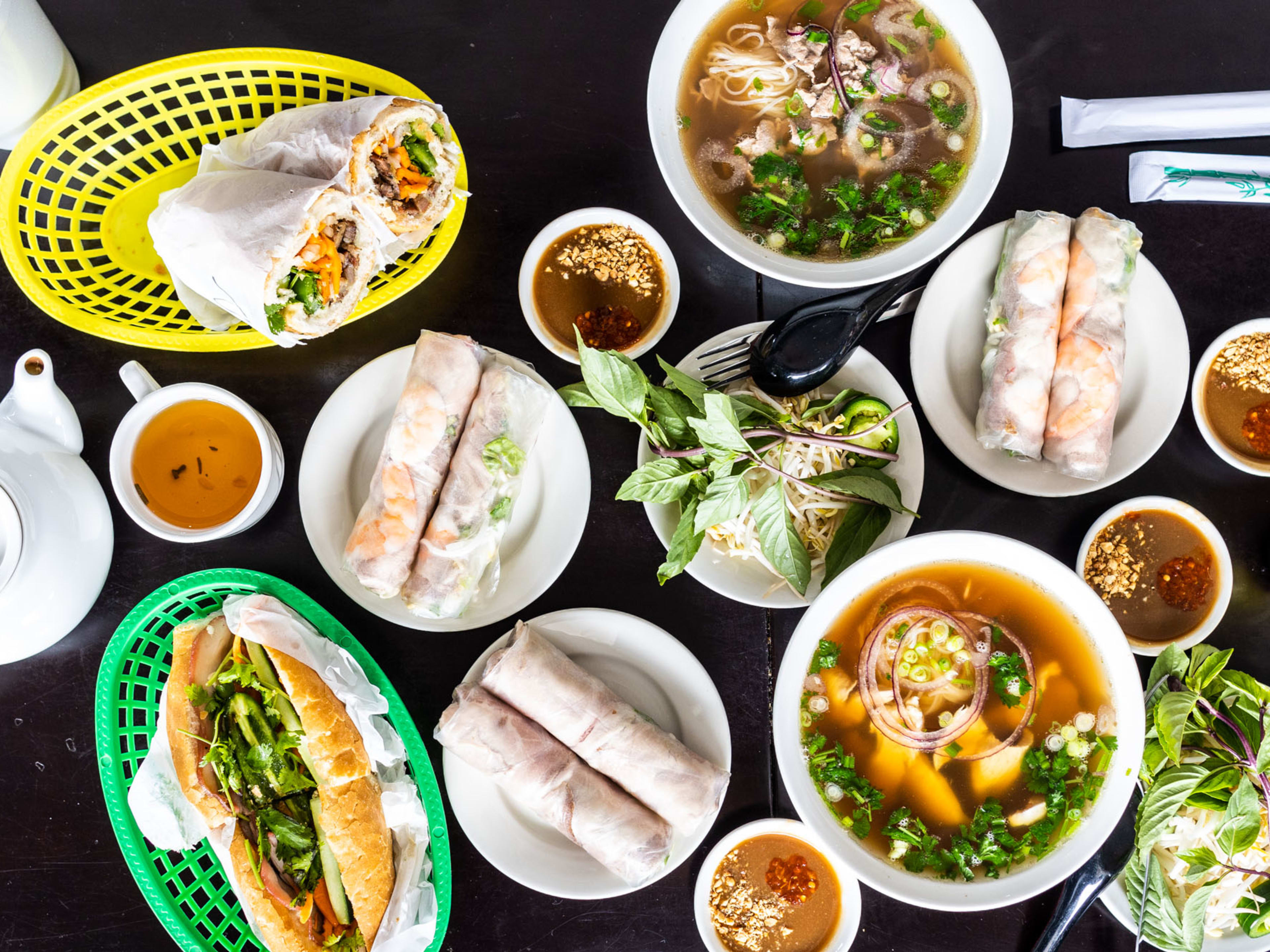 A variety of dishes from Cali Sandwiches & Pho served in white dishes and yellow or green baskets.