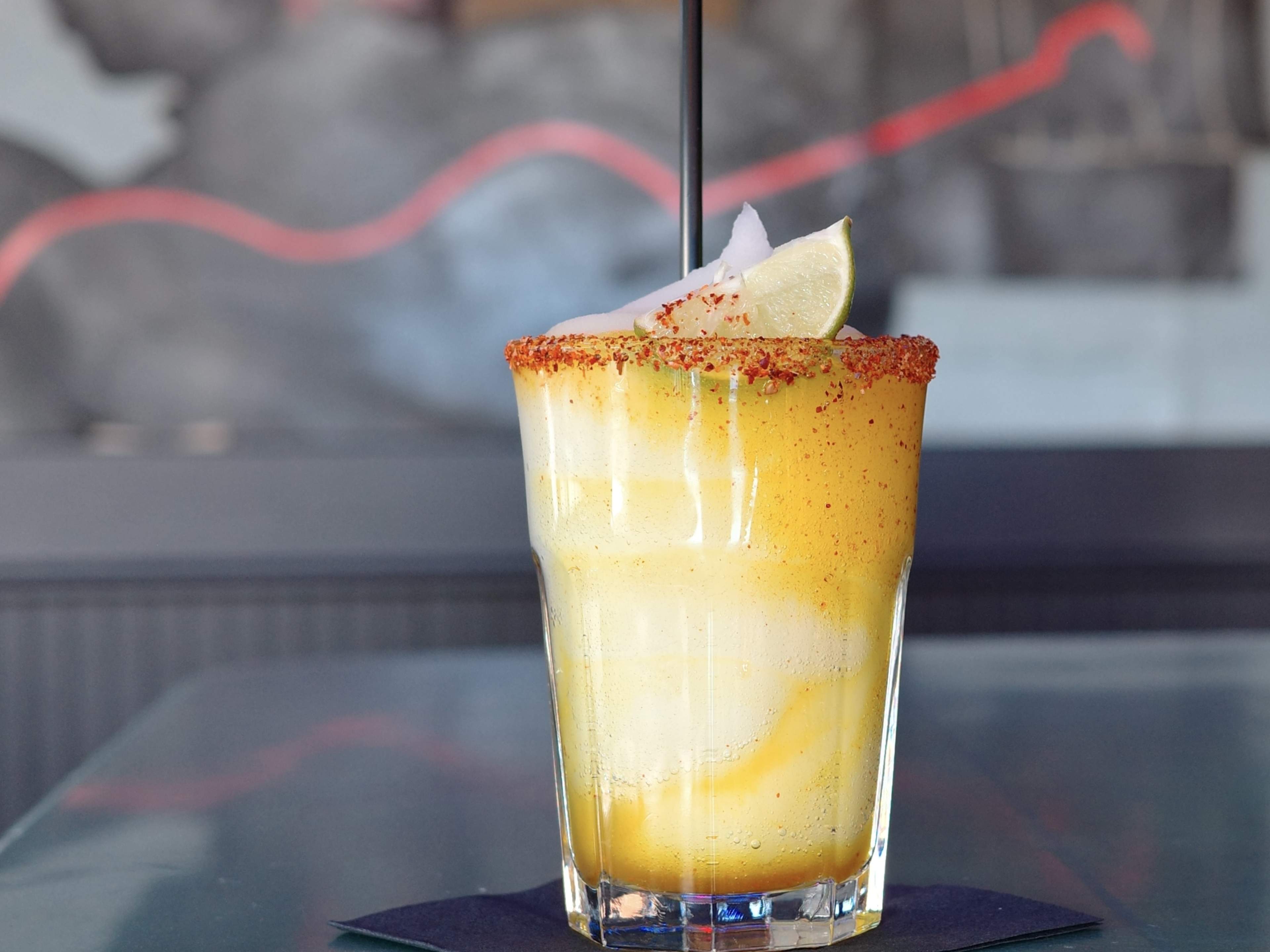 frozen margarita with a swirl of spicy mango in a glass with a tajin rim and wedge of lime