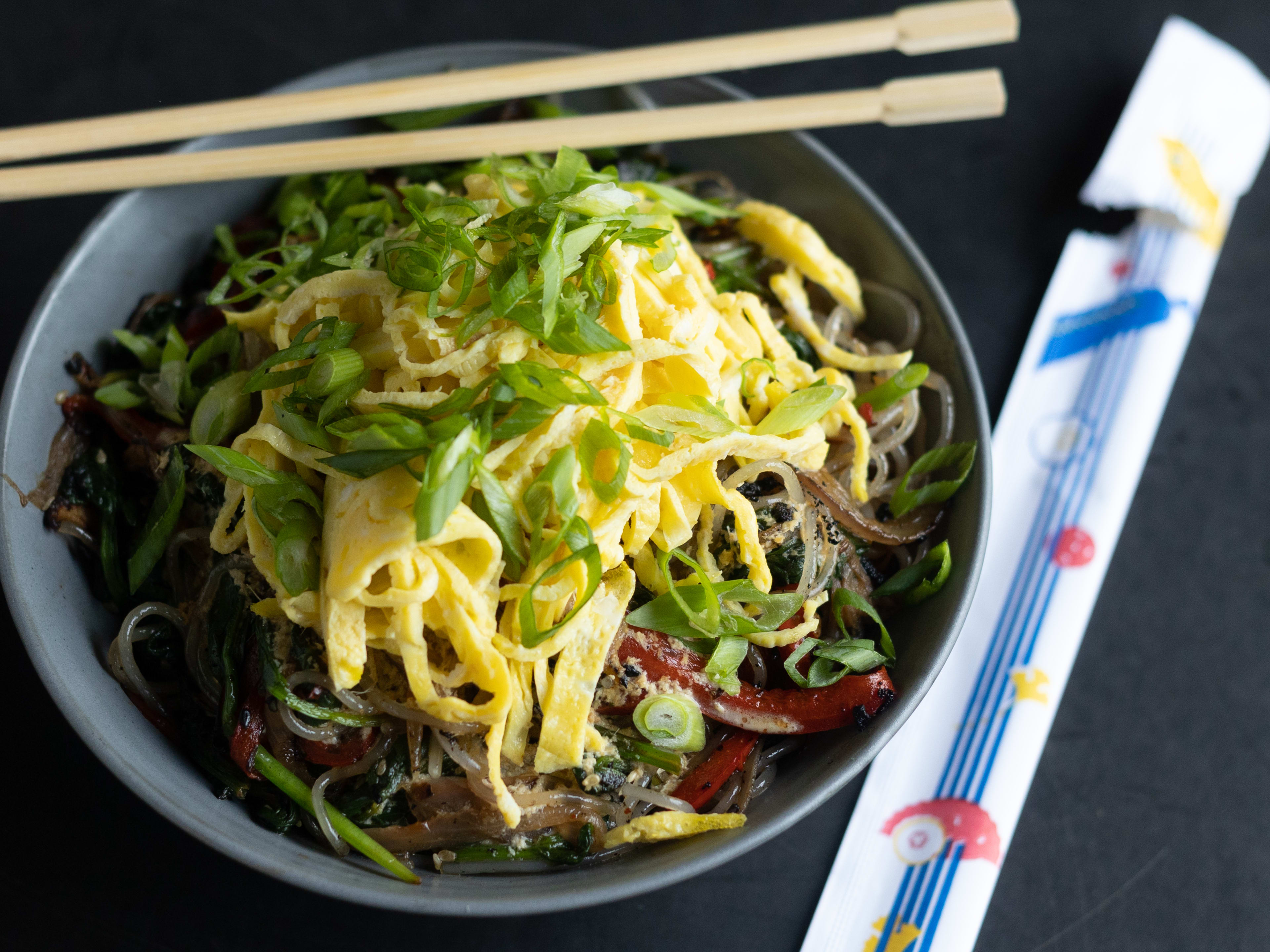 Chap chae noodles in a bowl with some chopsticks resting on top.