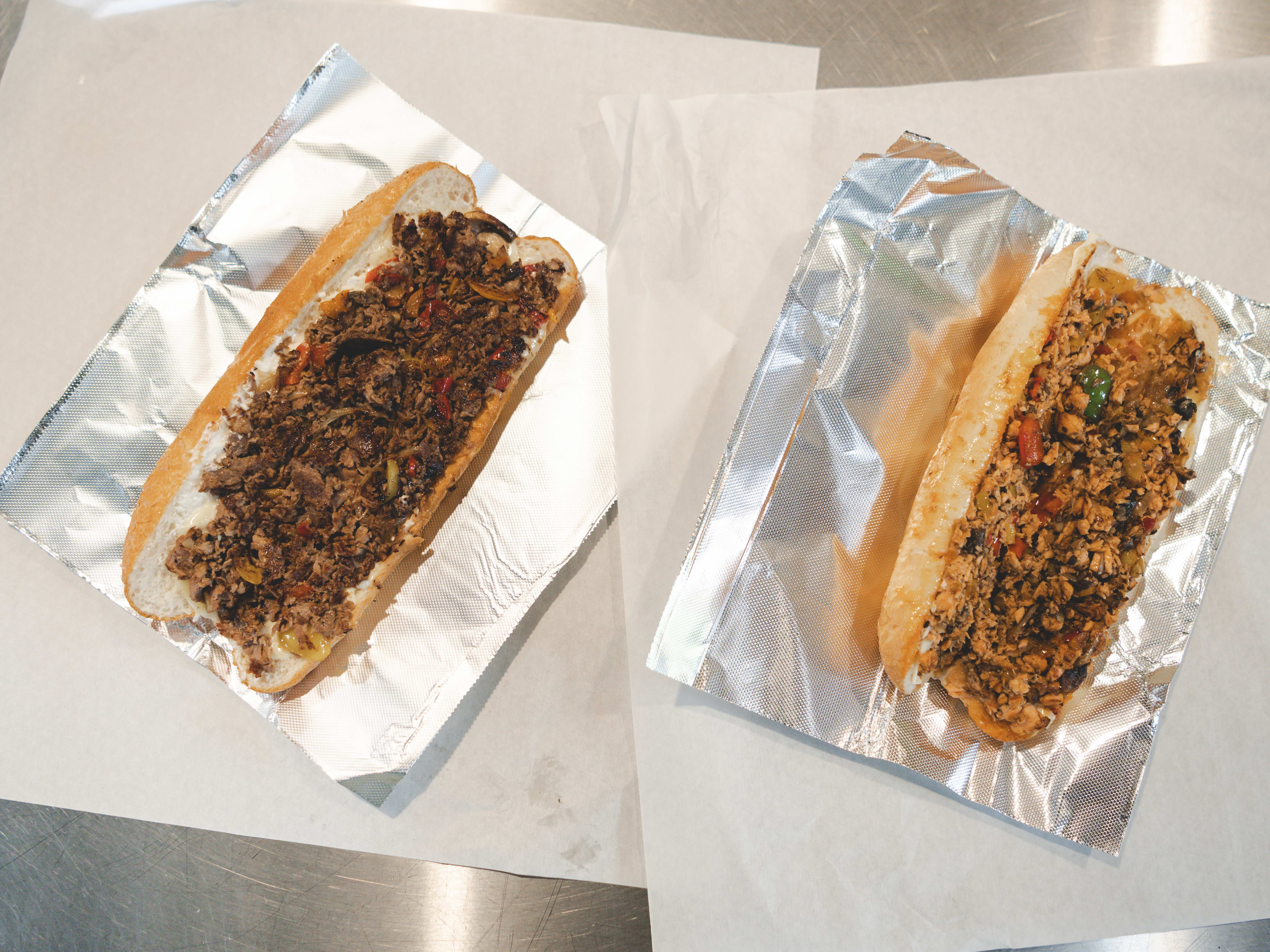 A ribeye cheesesteak and a salmon cheesesteak sit side by side on foil.