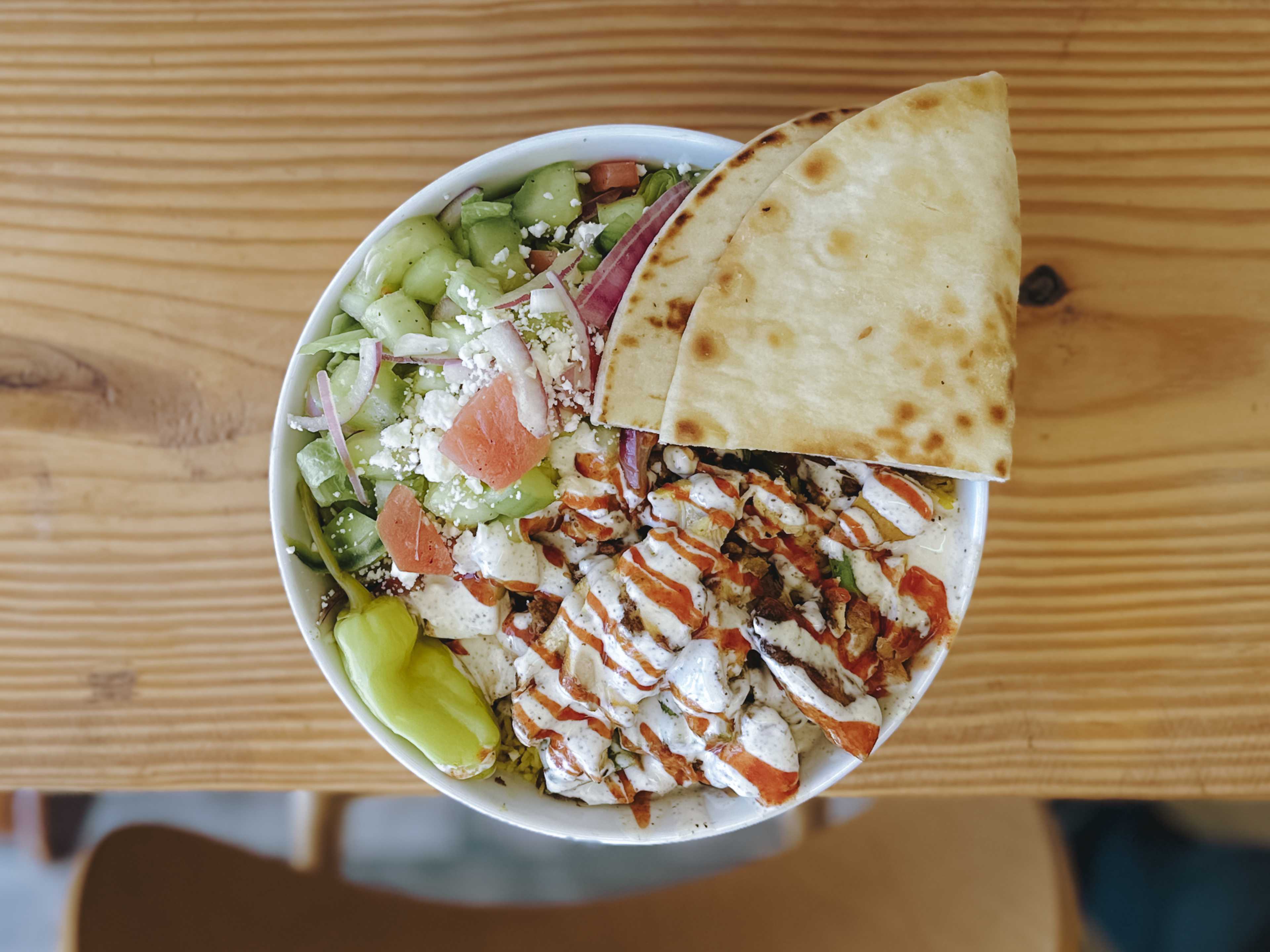 chicken shawarma served with yellow rice, lettuce, peppers, and tzatziki-like white sauce.