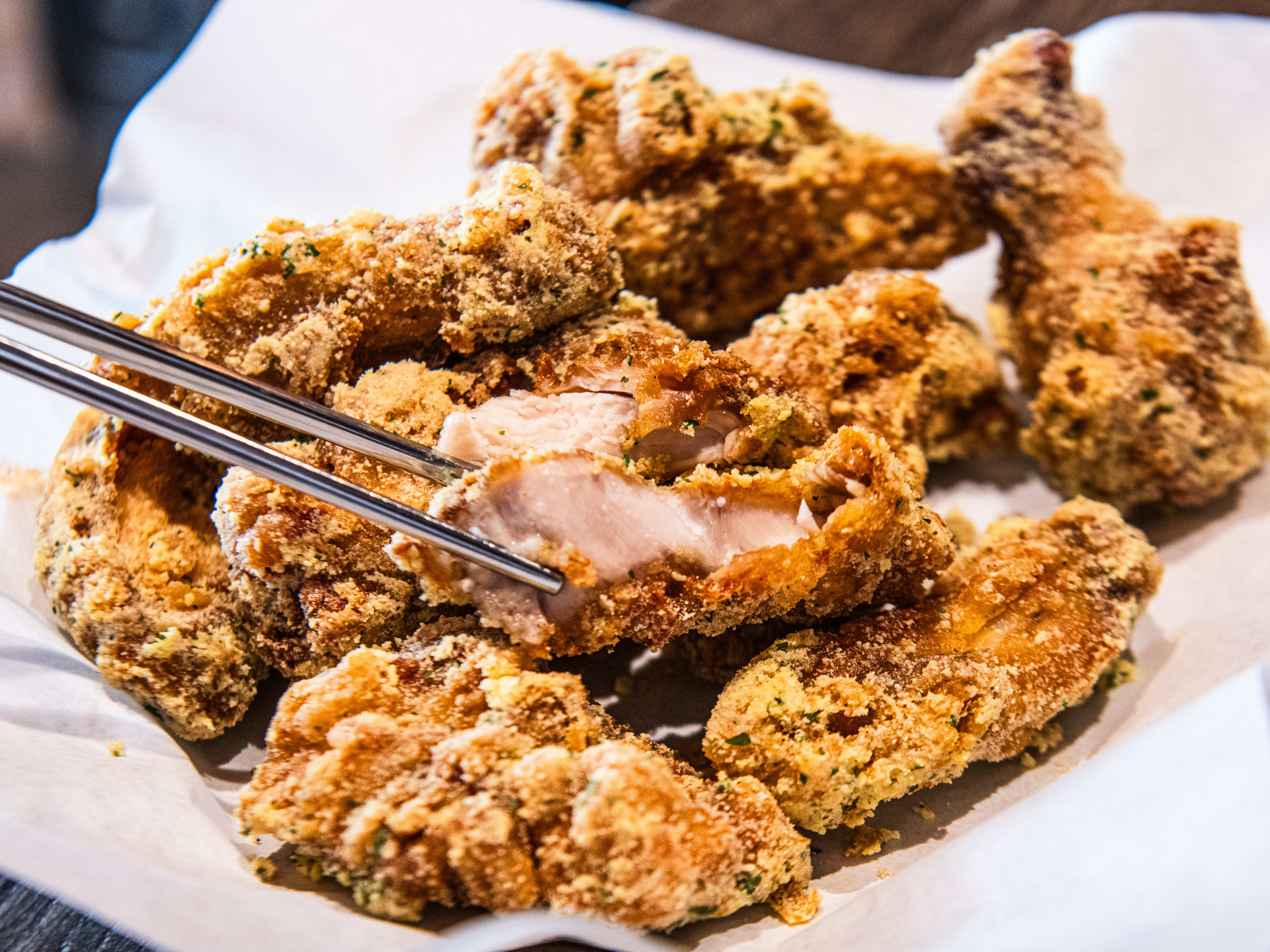 A basket of honey butter fried chicken. One piece is bitten into and held by silver chopsticks.