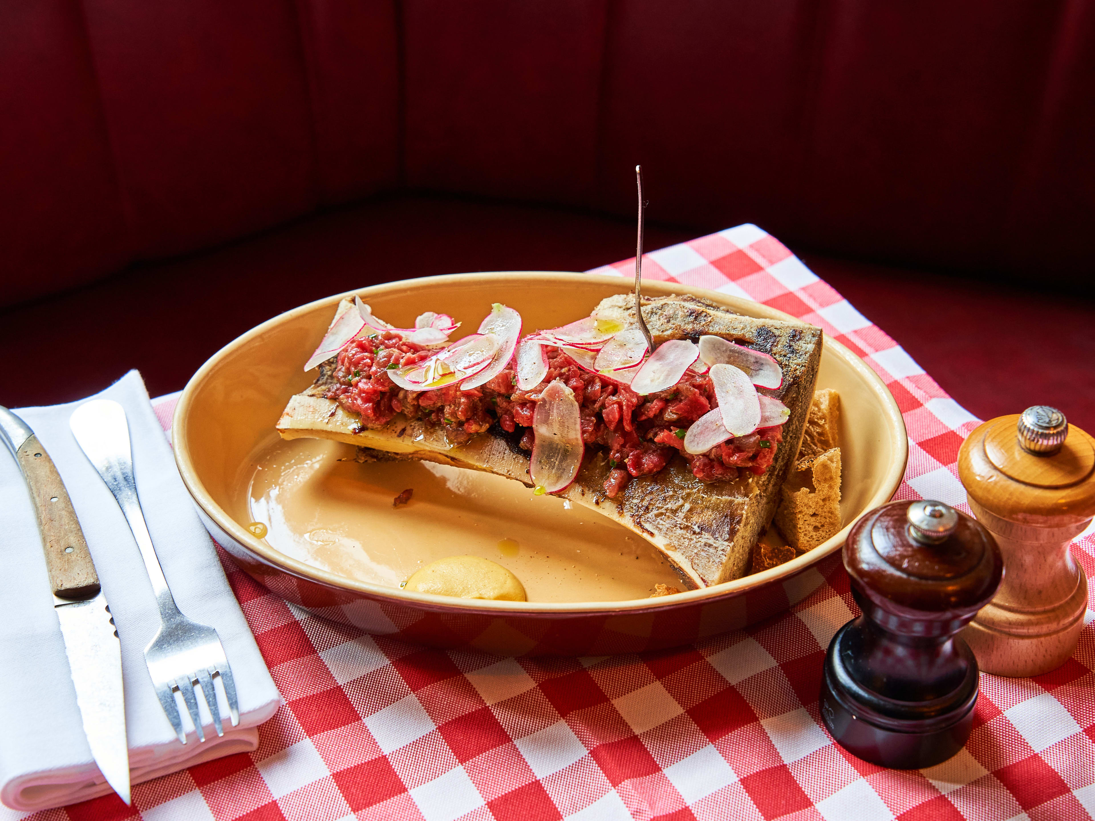 Beef tartare with bone marrow plated inside bone on red checkered tabecloth at Chez Marius