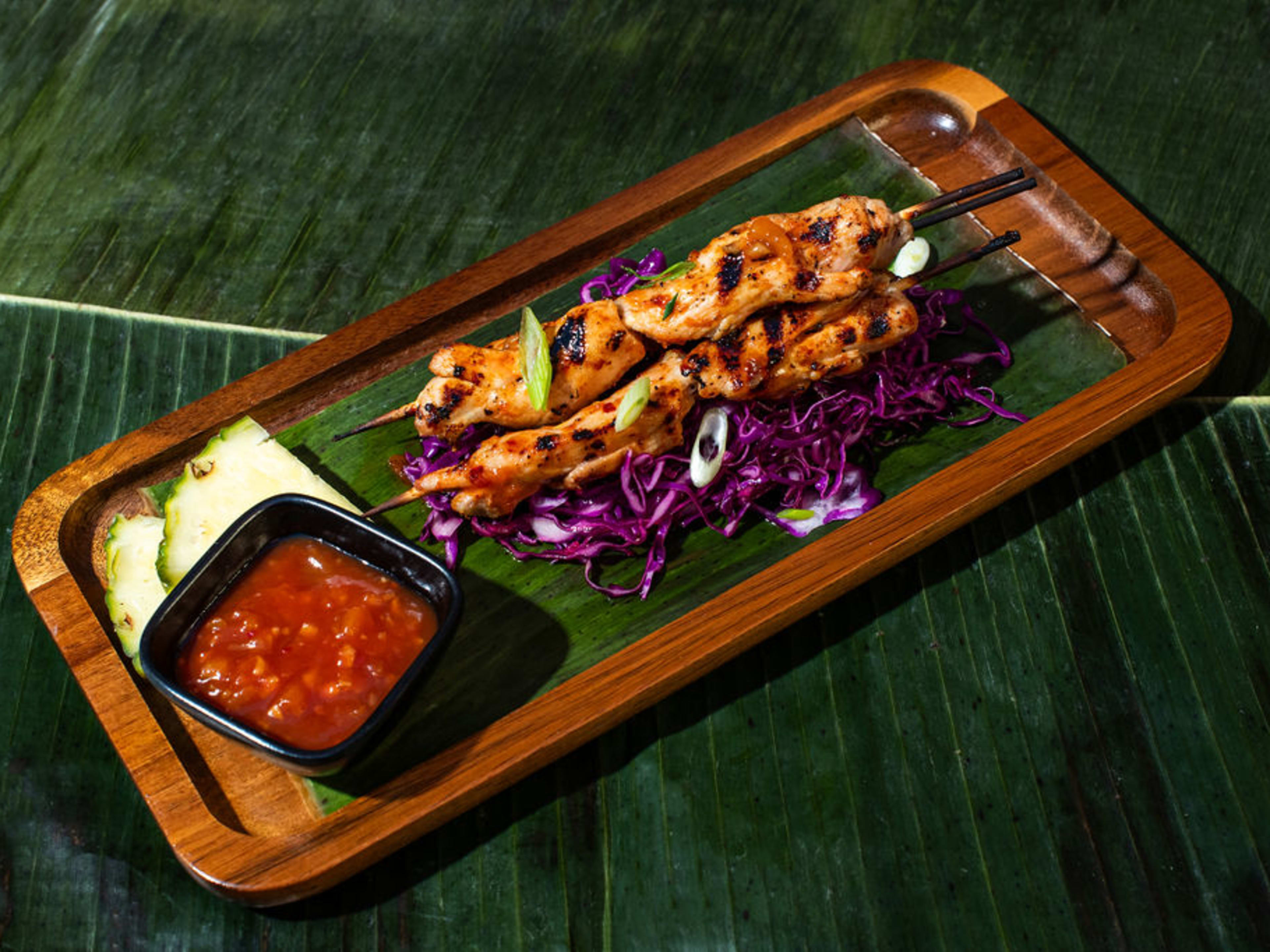 chicken inasal skewers on bed of cabbage served next to sauce