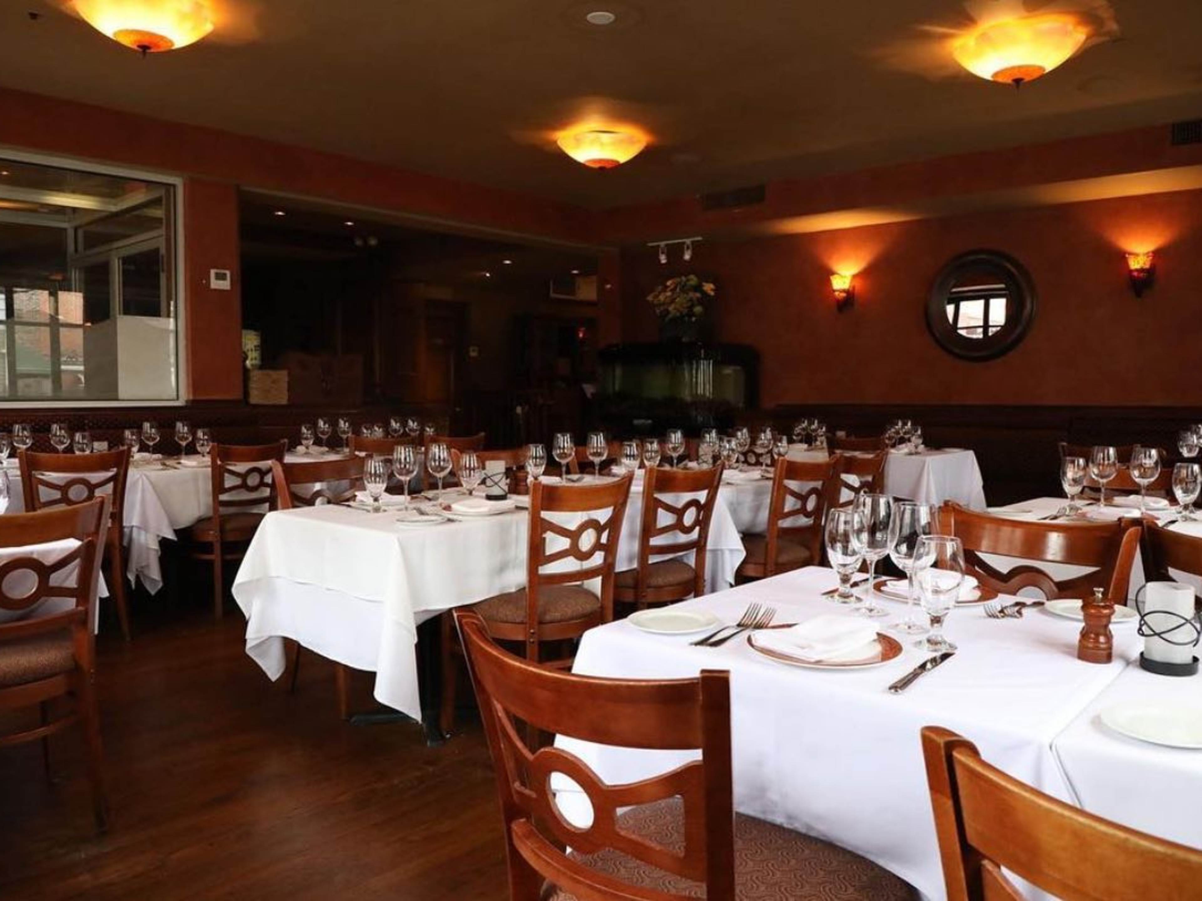 A plain yet fancy dining room with tables covered in tablecloths.