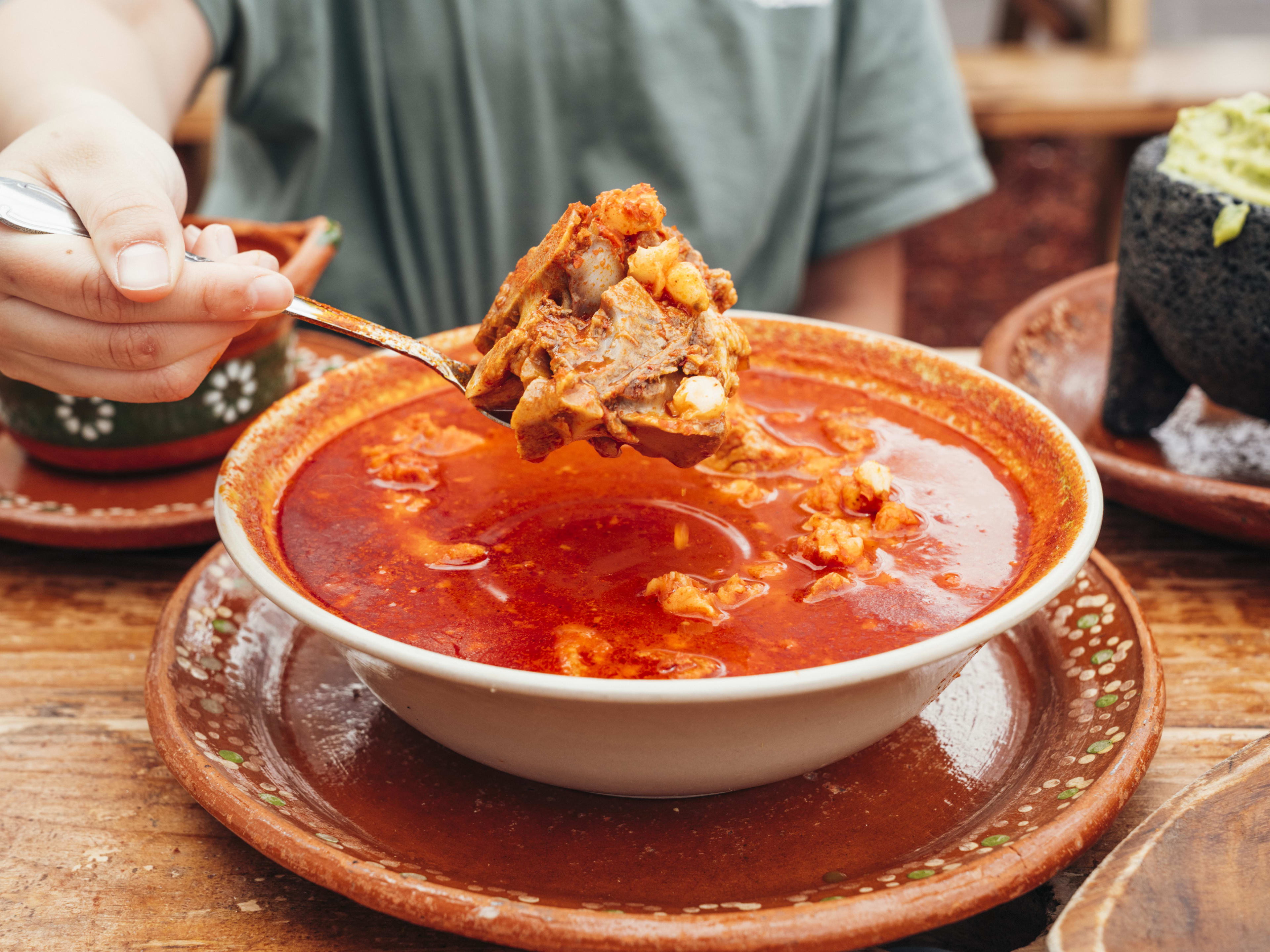 pozole rojo in bowl, person holding up spoon with big meat chunk