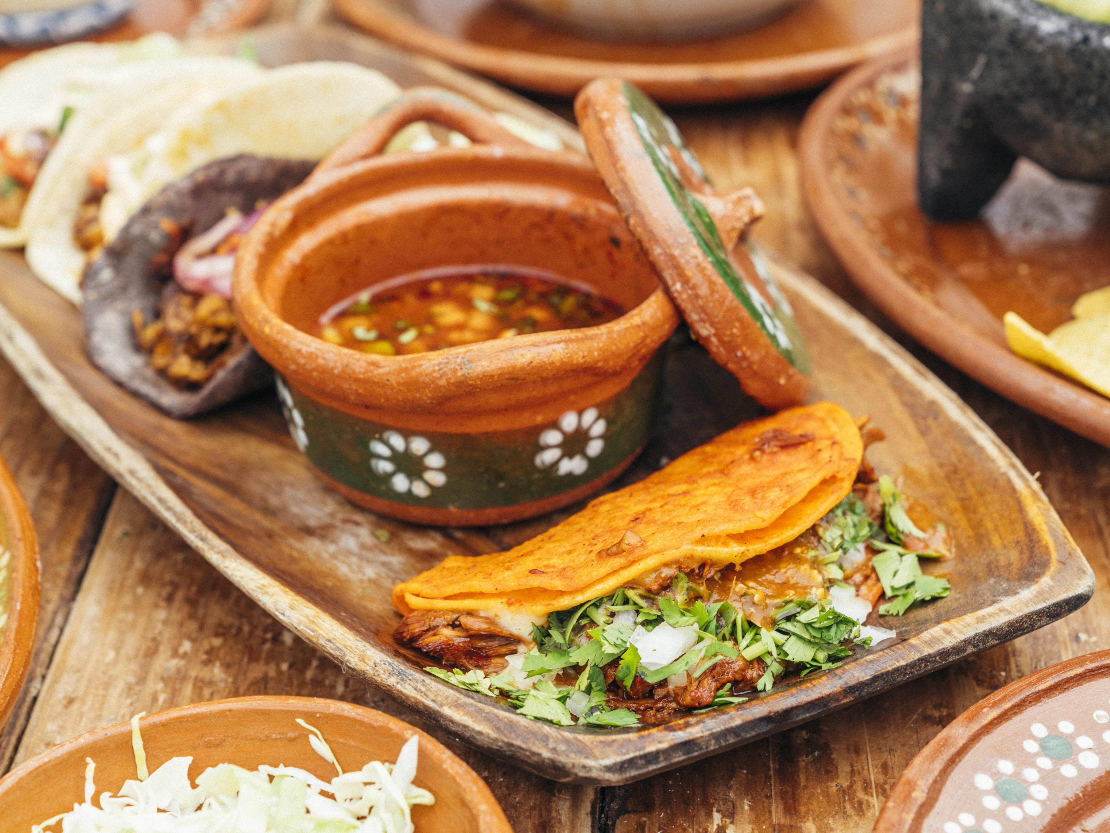 quesabirria taco with consomme dipping liquid in small ceramic crock