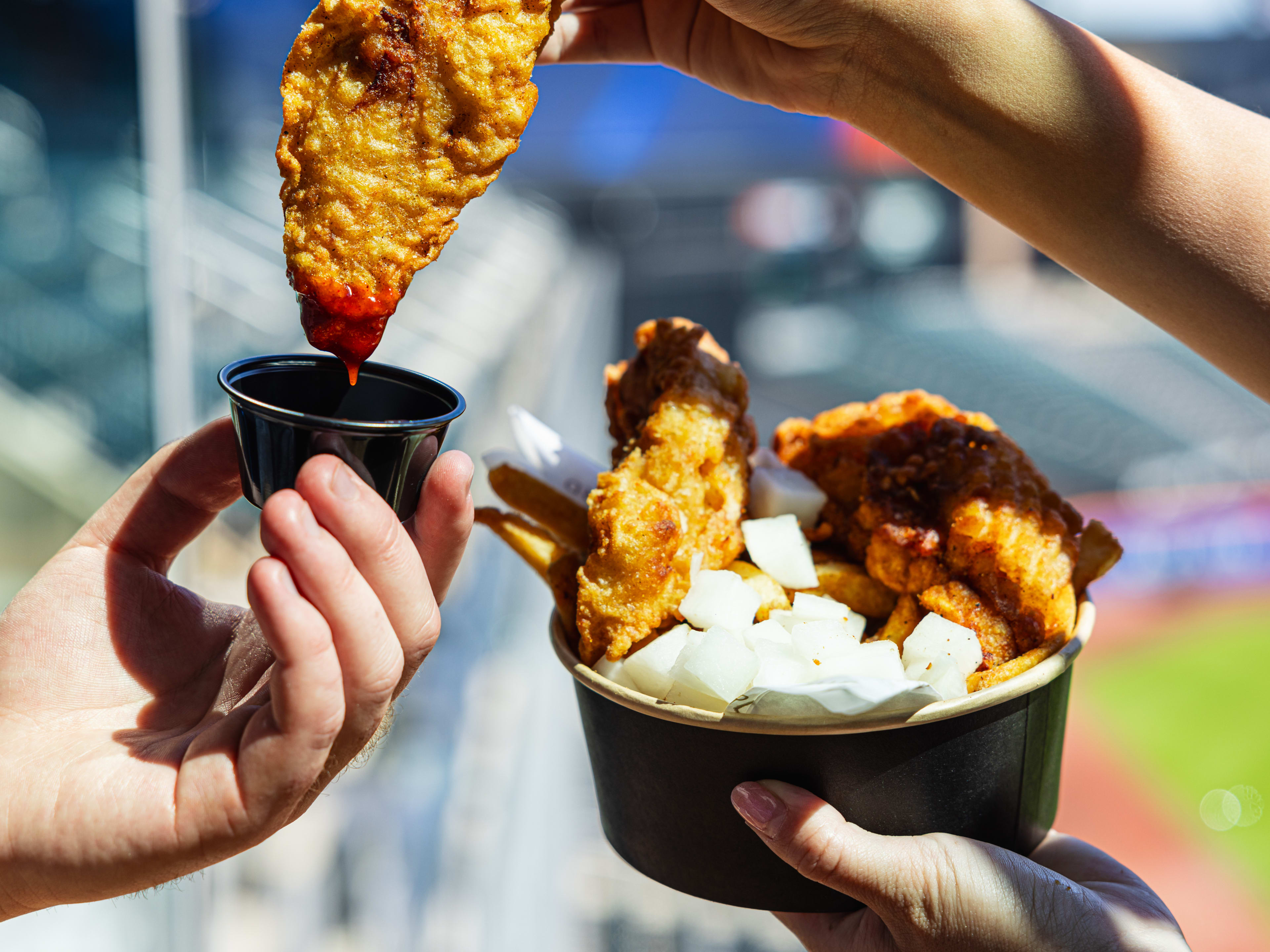 fried chicken being dipped into a gochujang barbecue sauce with pickled daikon radish