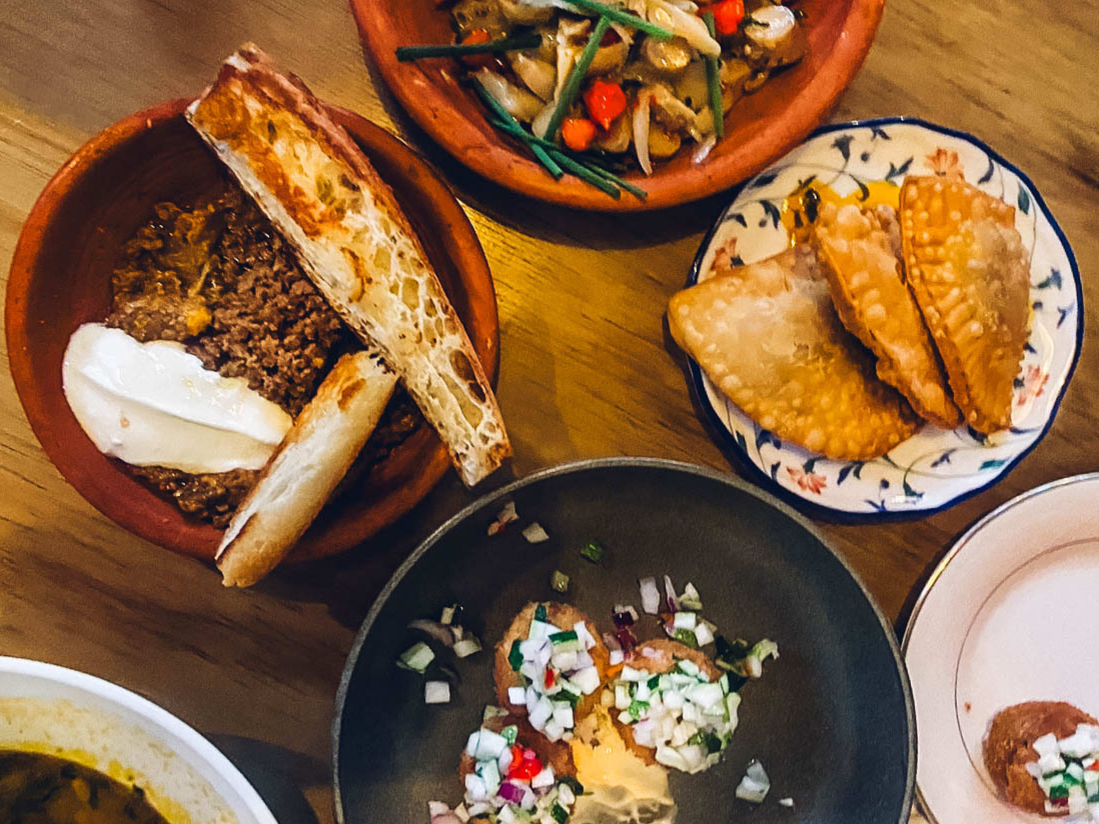 A table filled with mismatched plates of meat, vegetables, and arepas at Cocina al Fondo, a restaurant in San Juan