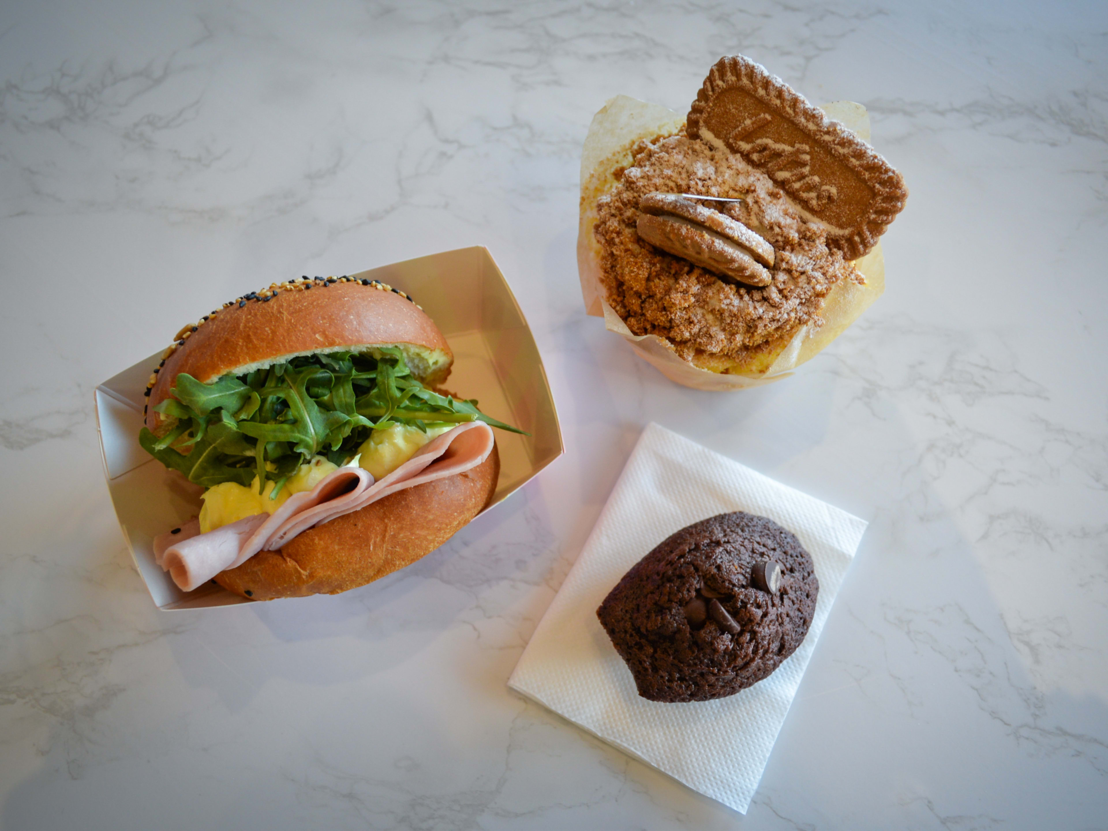 Spread of biscoff cupcake, brownie, and ham and egg sandwich with arugula on marbled counter.