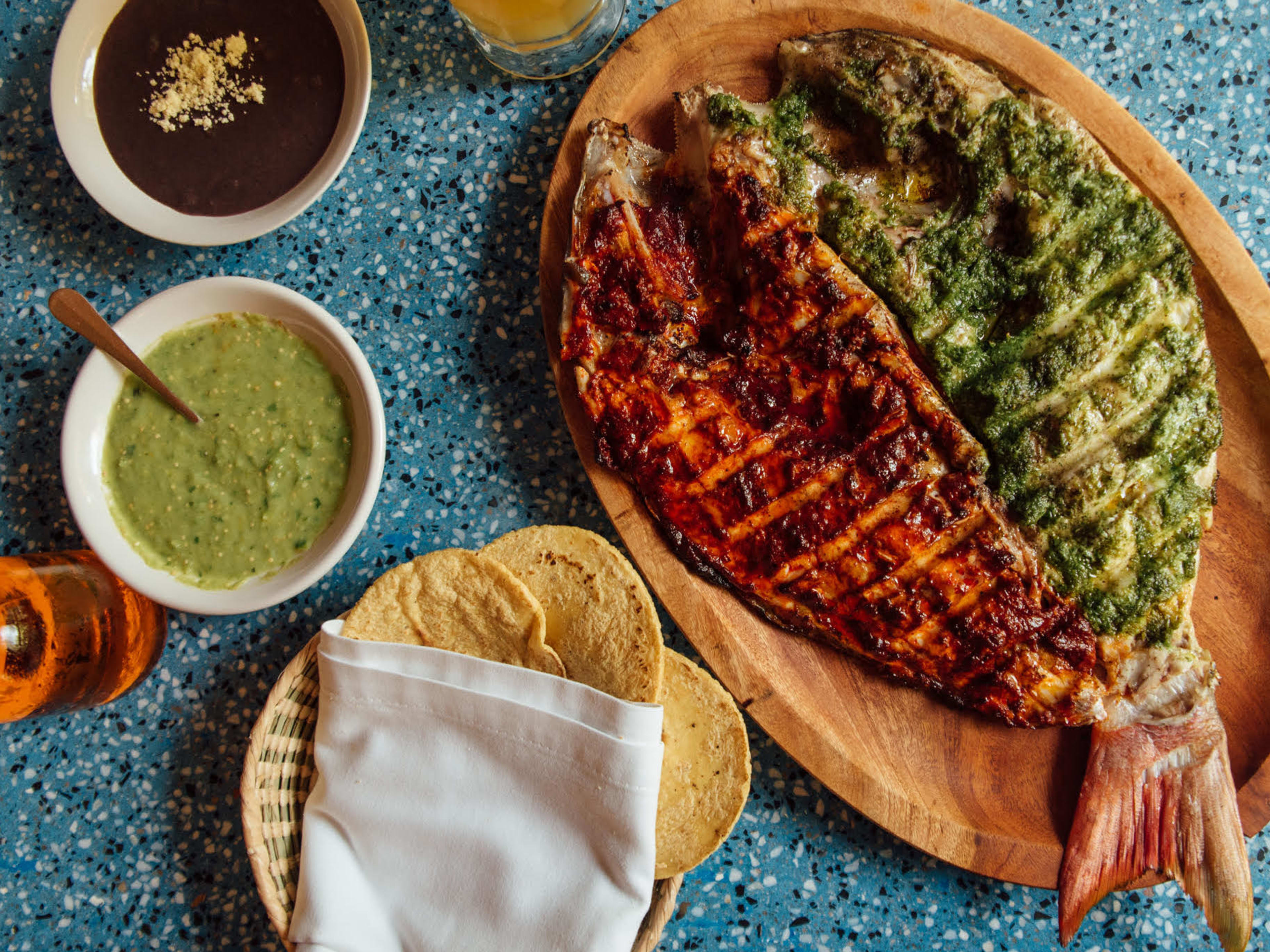 A plate of fish covered in a red and green sauce, served with tortillas and salsa, at Contramar in Mexico City