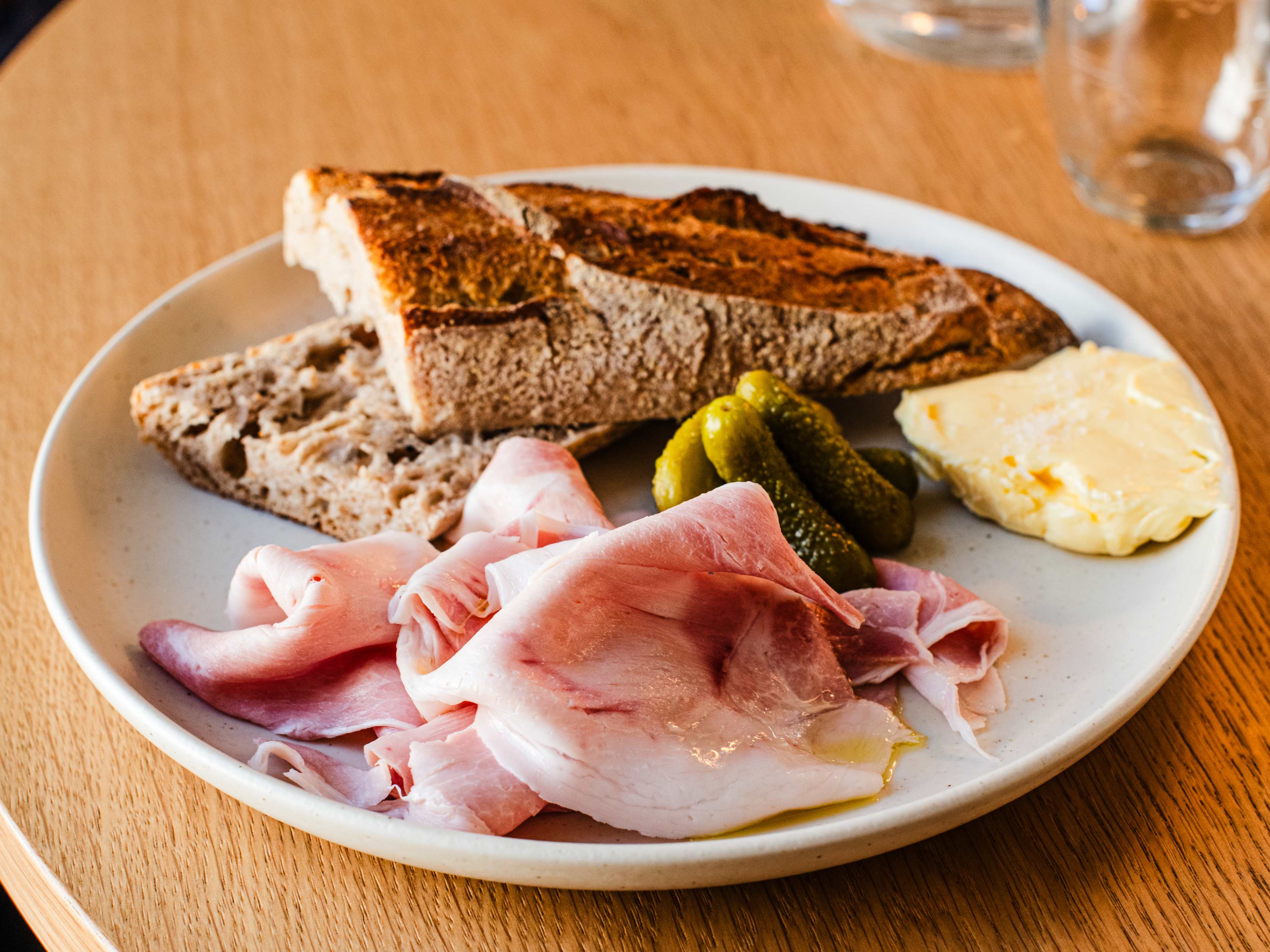 A plate of baguette, ham, pickles, and butter.