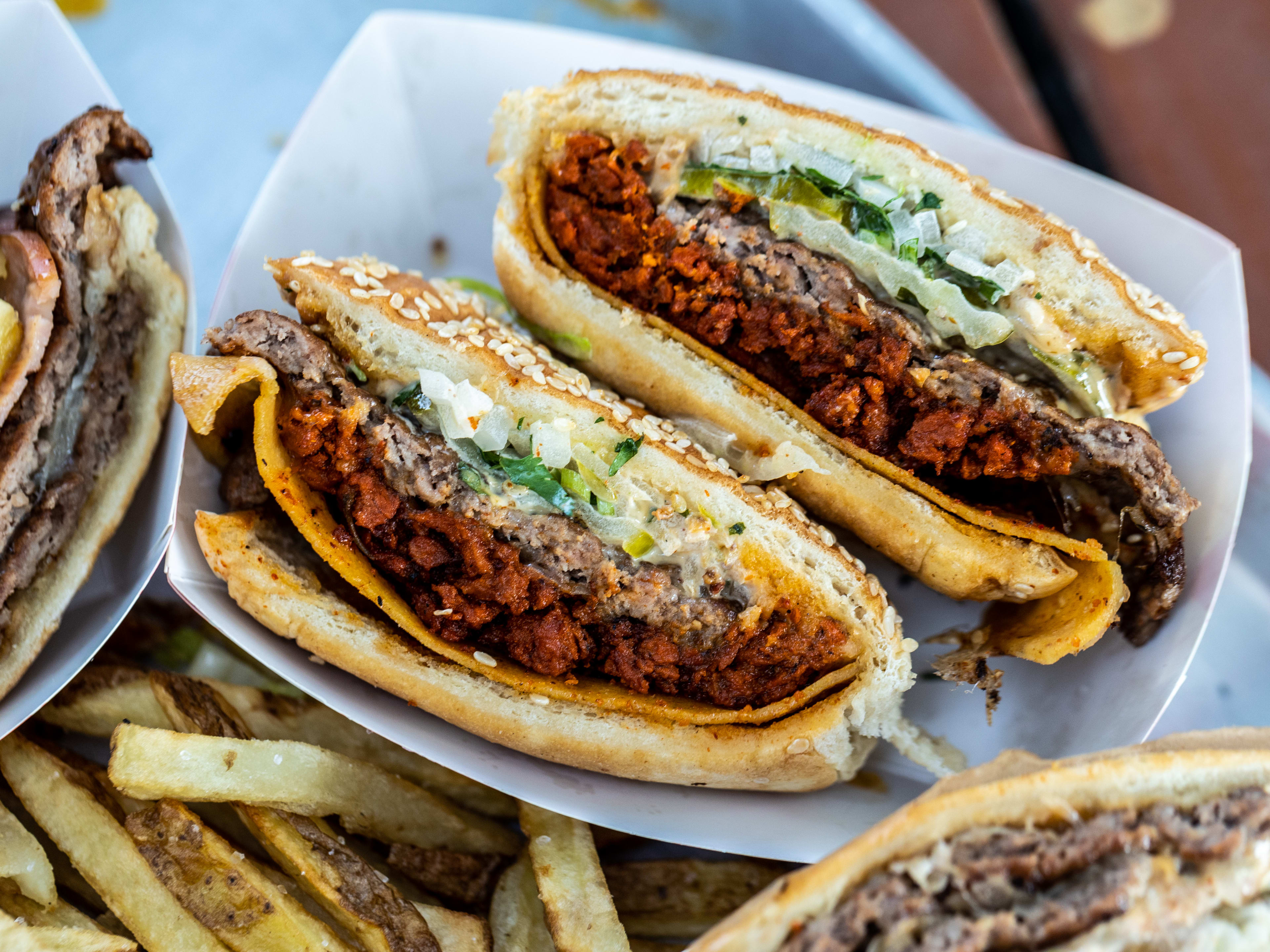 The Campechana from Cuantas Hamburguesas but in half in a paper takeaway basket with other burgers and fries on the side. It has has a beef patty and a Mexican chorizo patty on it.