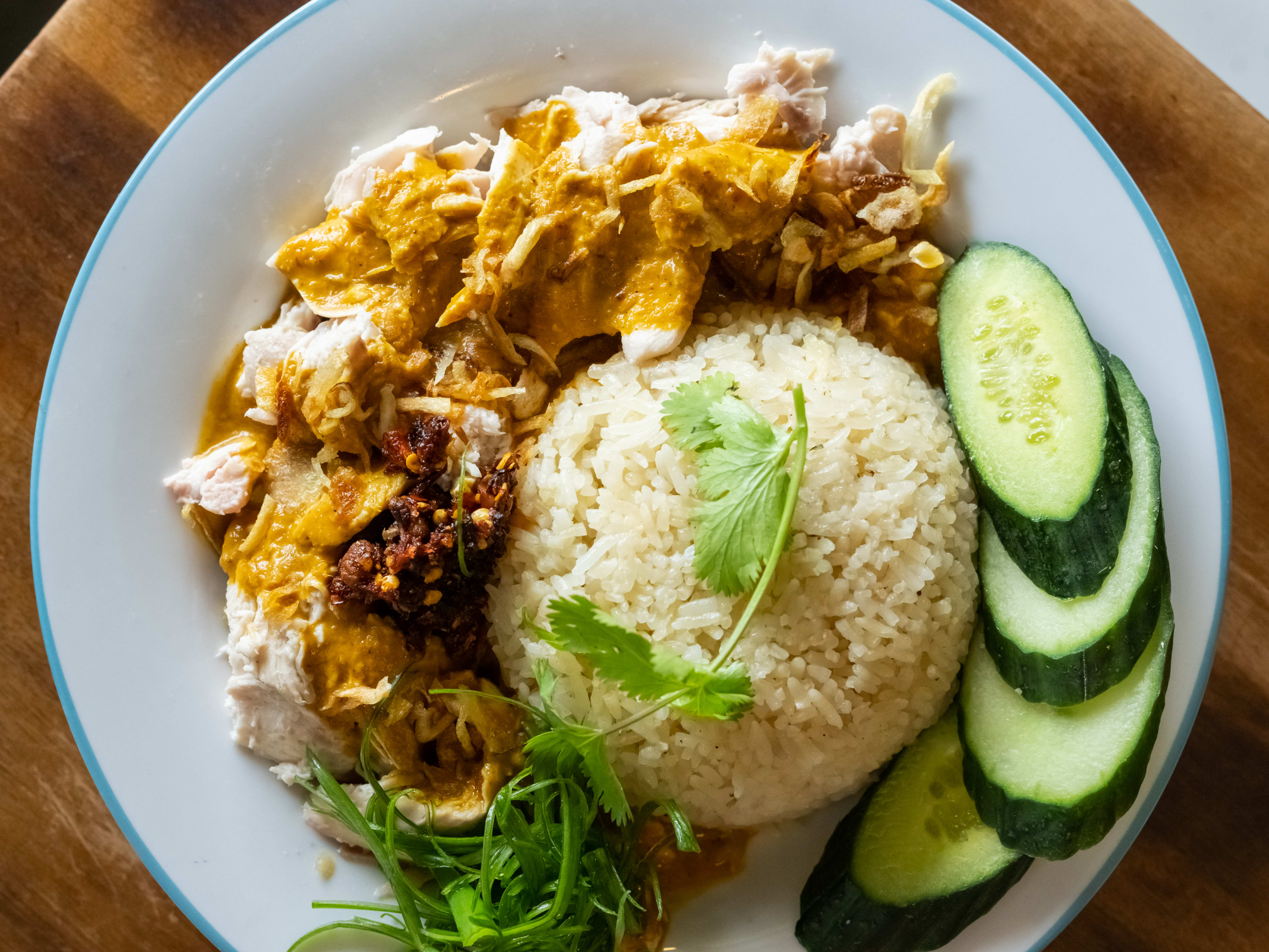 Plate of curry chicken with rice and raw cucumbers