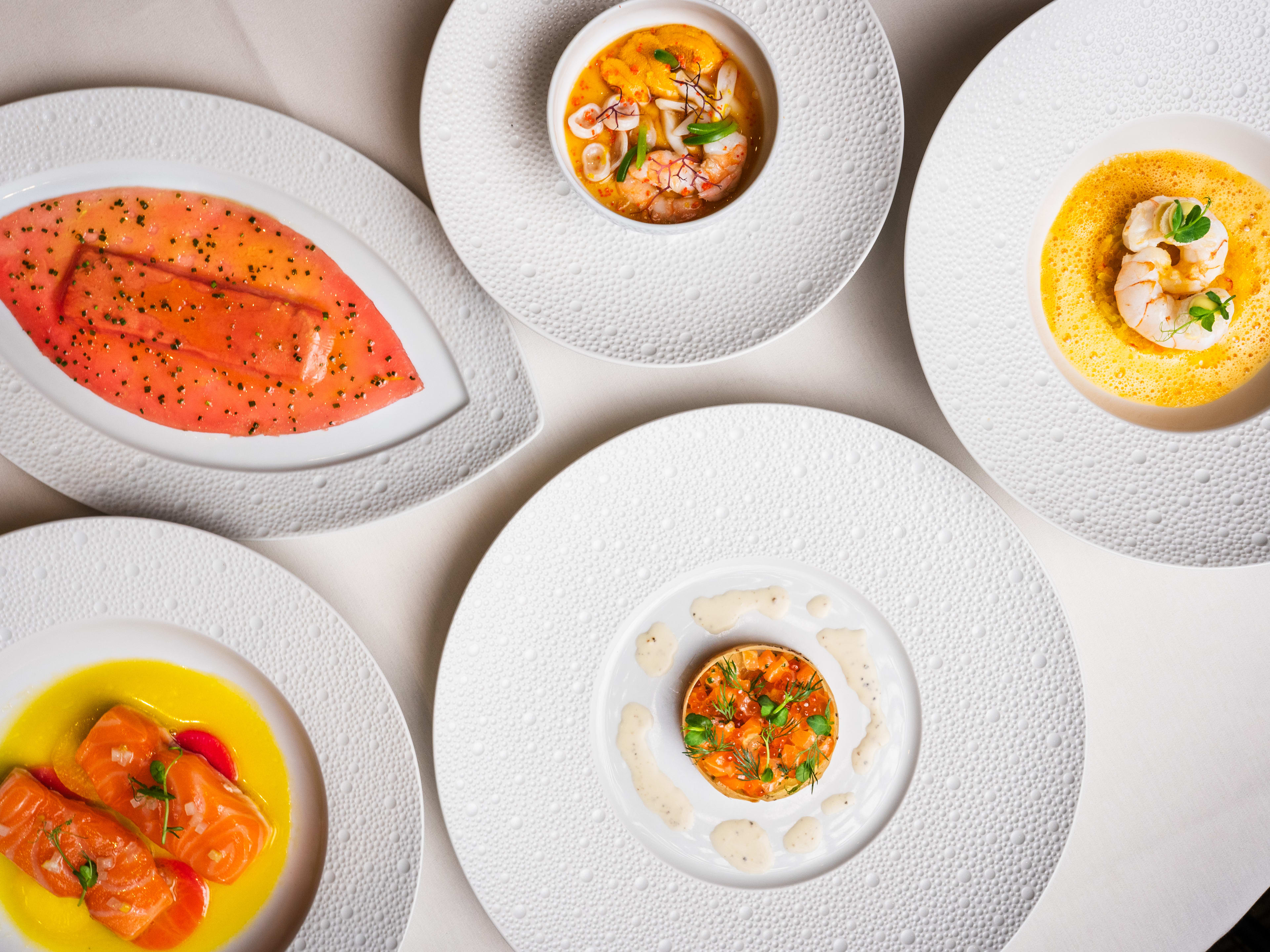 A spread of small, fancy seafood dishes on a pristine white tablecloth.