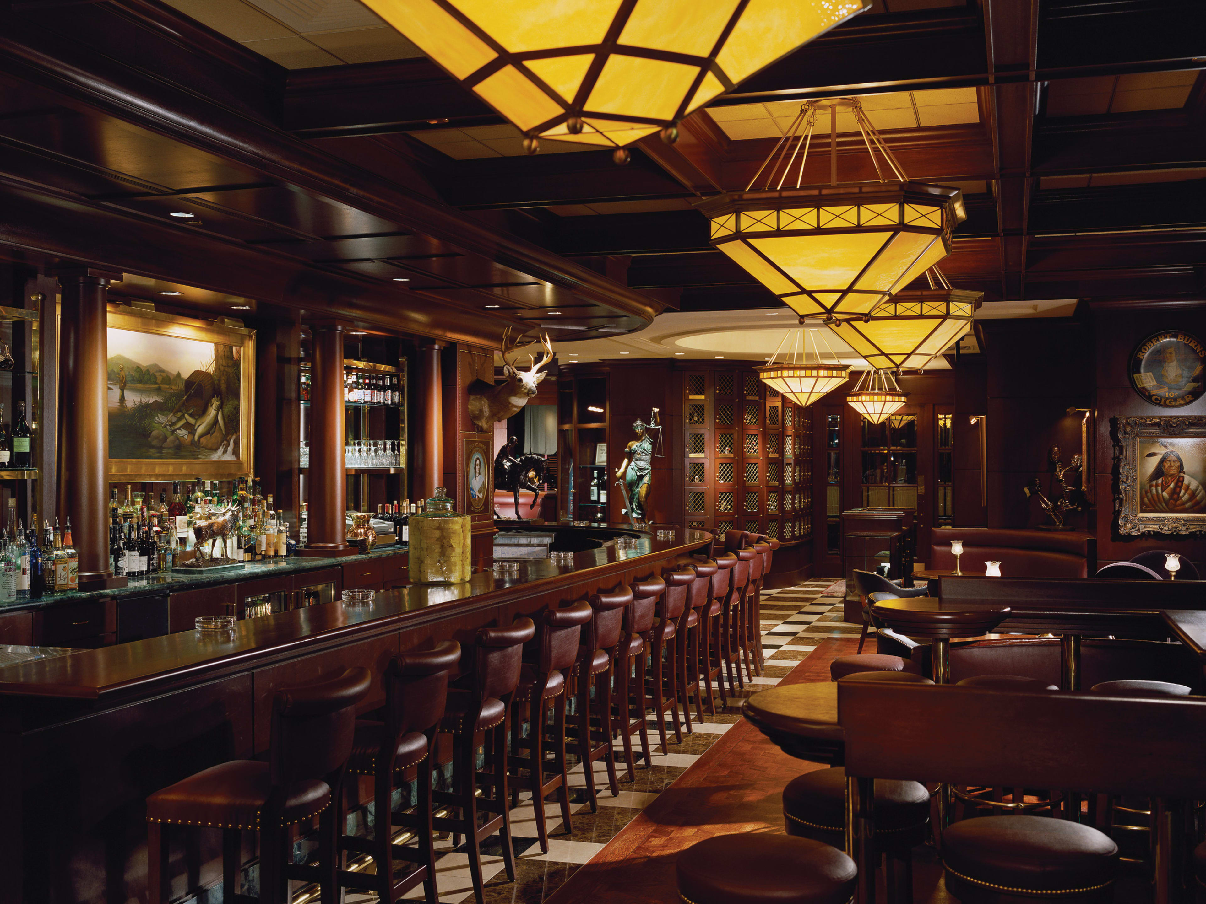 Dark wooden and leather steakhouse interior with bar and dim chandeliers.