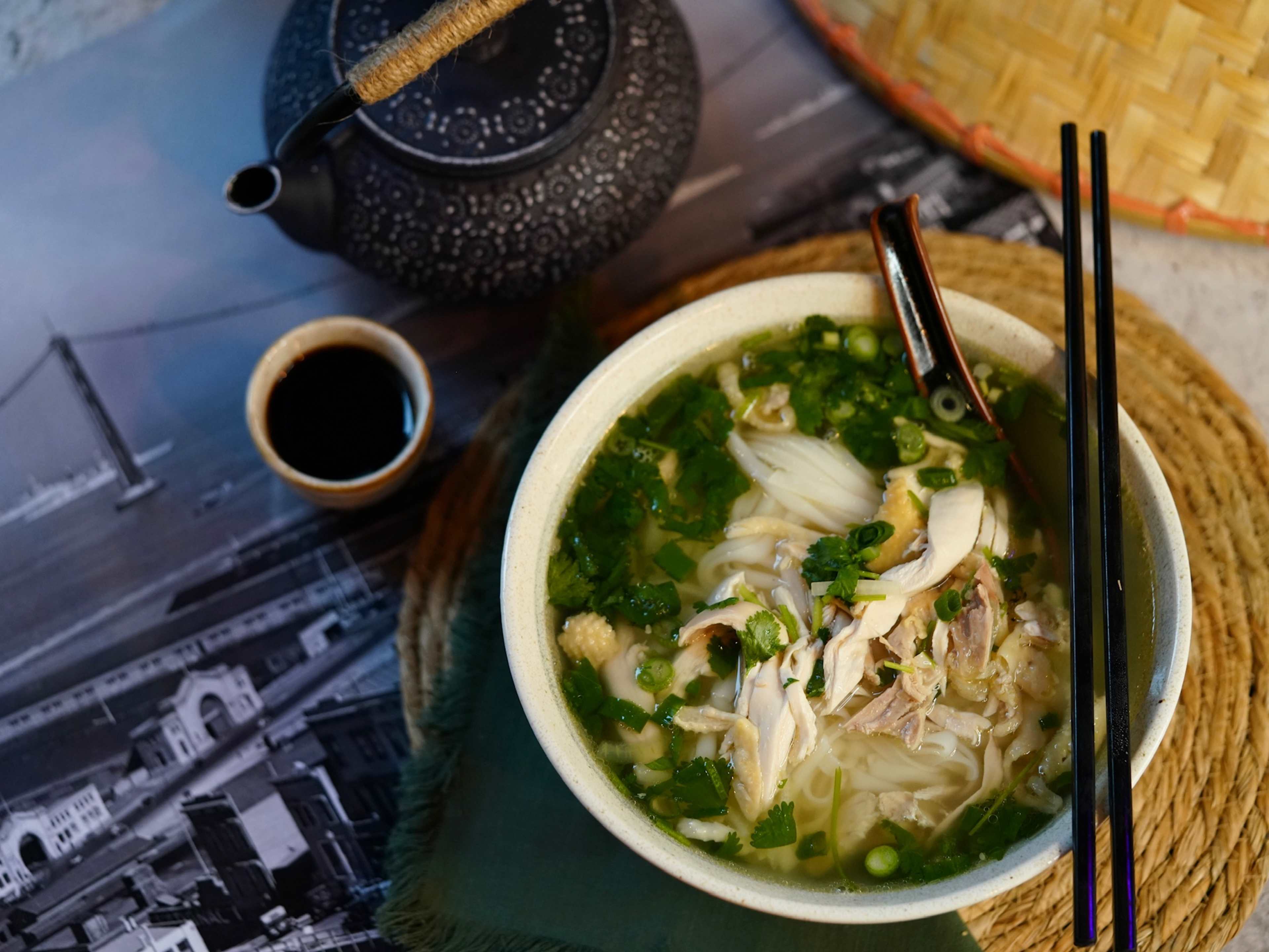 bowl of chicken pho next to tea pot and cup