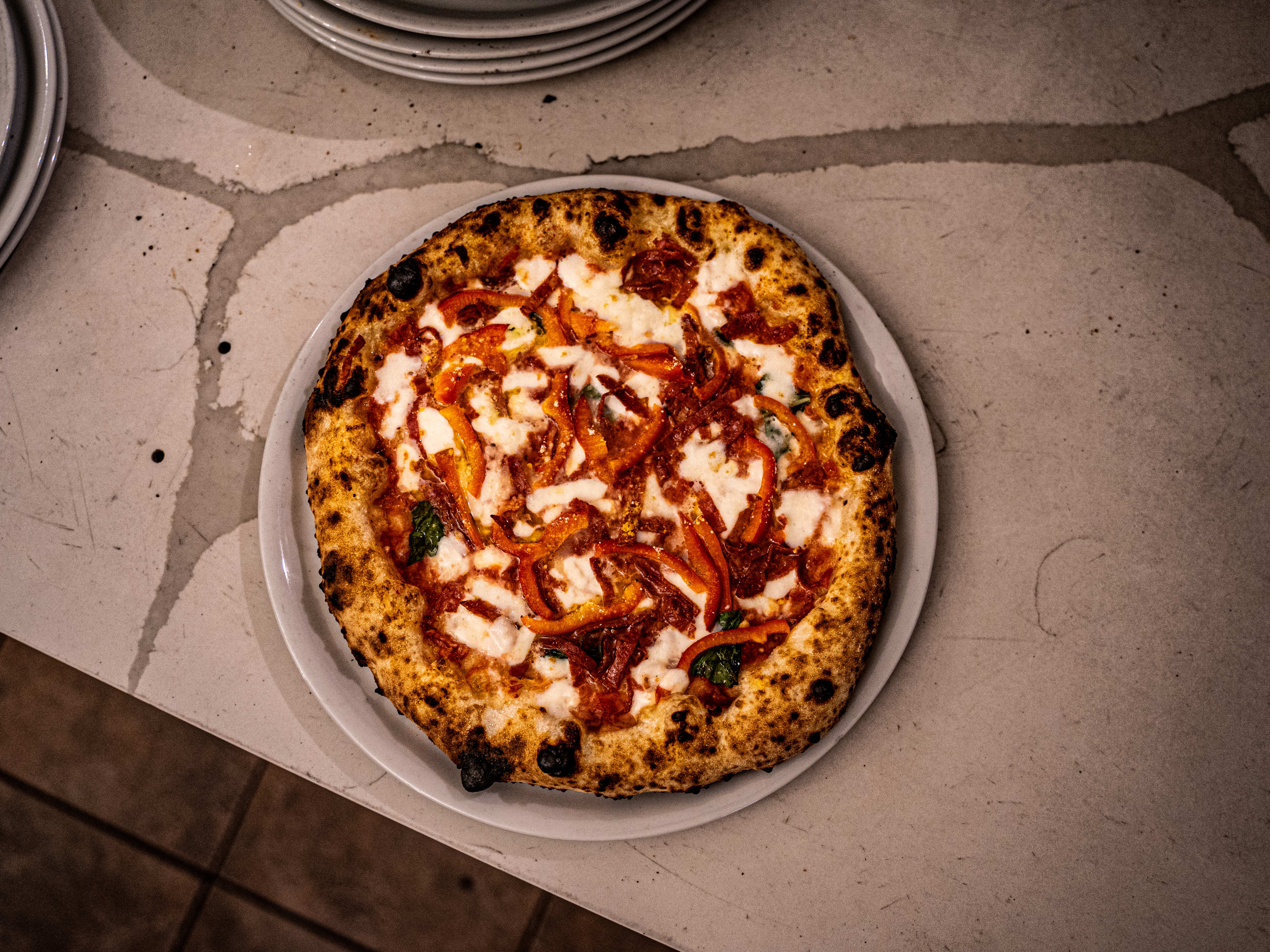 Pizza with peppers, sauce, and mozzarella, with charred crust on a concrete counter.