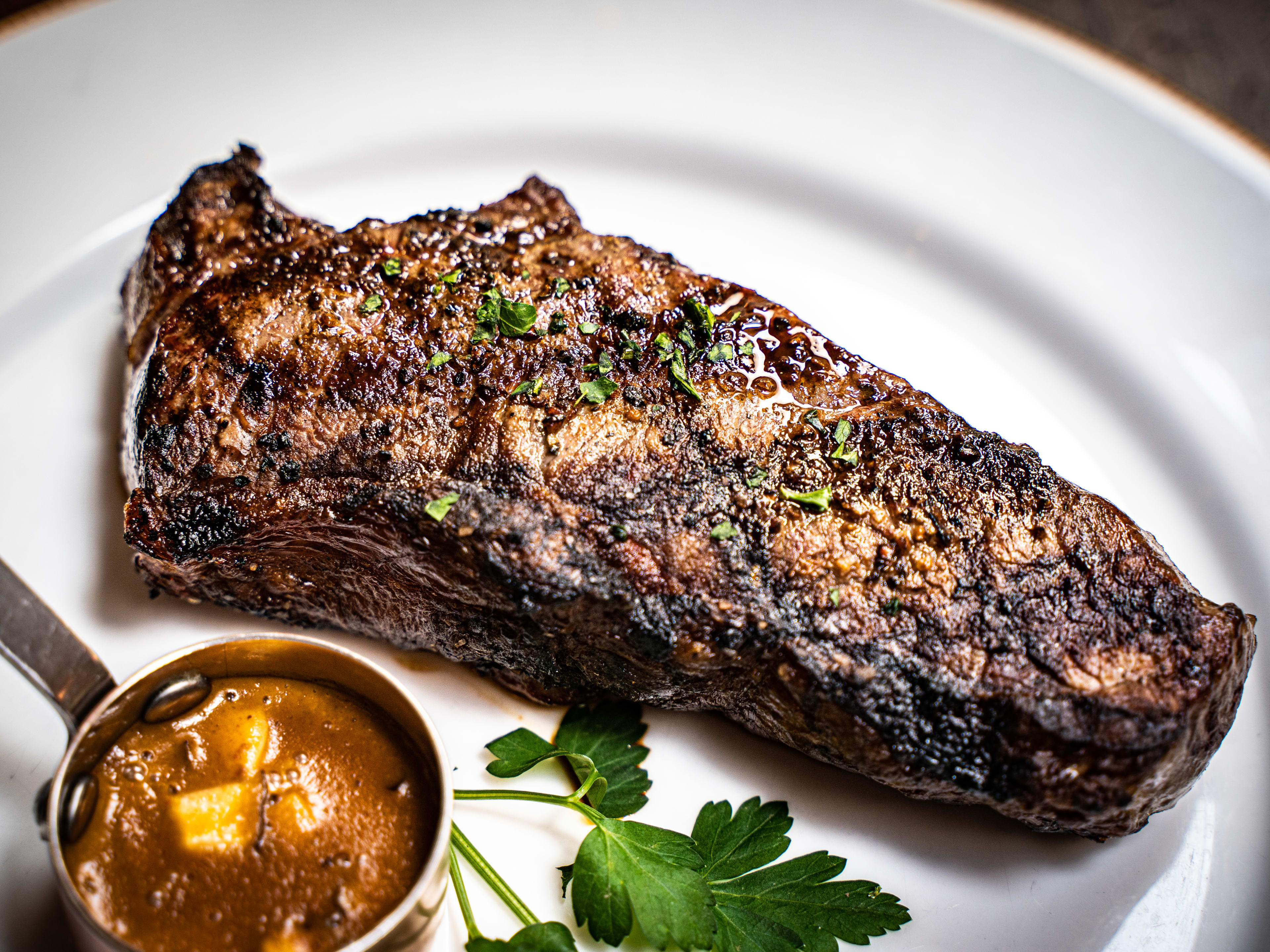 glistening steak with char grill marks and small pot of sauce