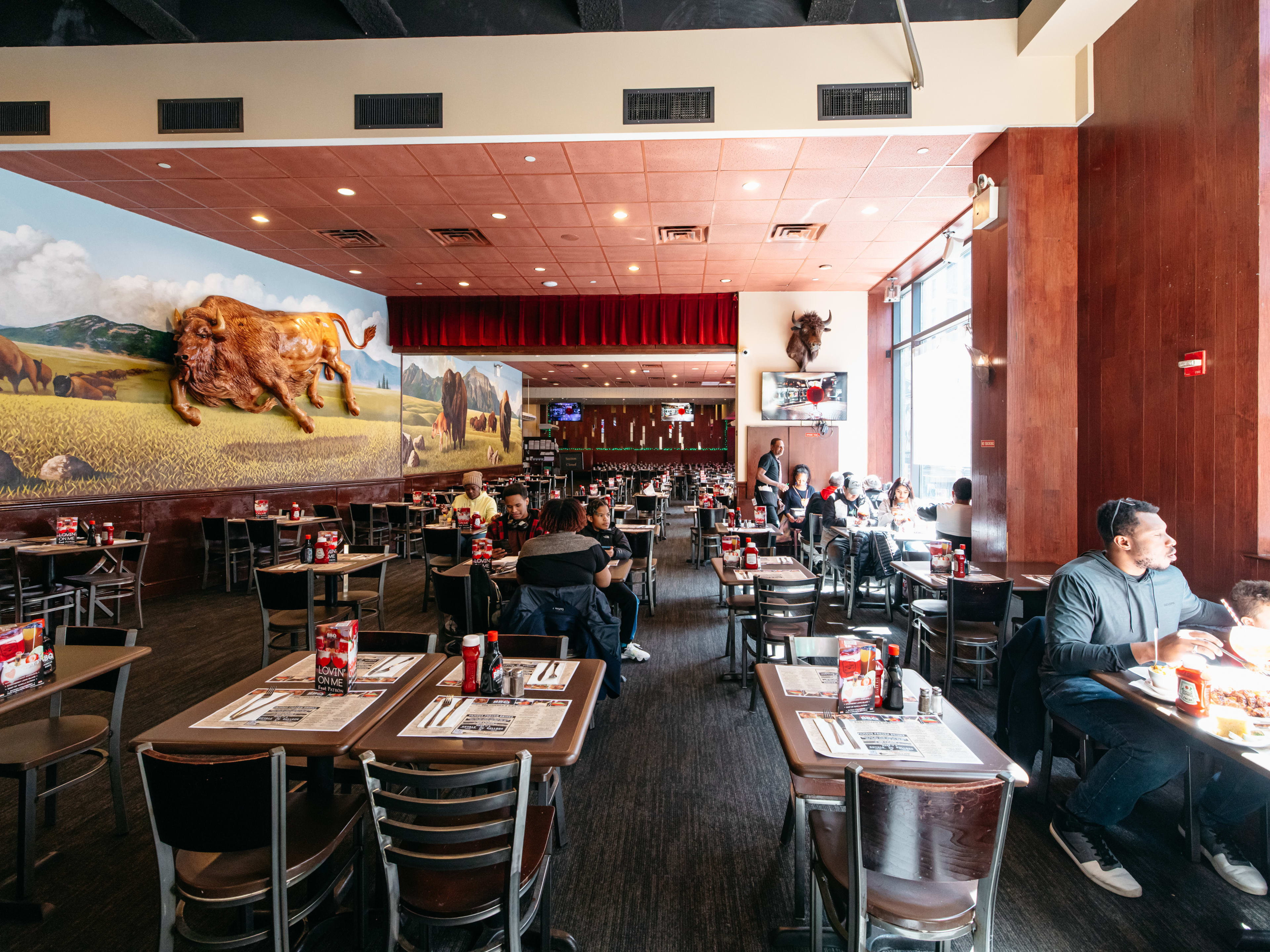 The interior of Dallas BBQ in Times Square, a big restaurant with many tables and a mural of buffalo on the wall.