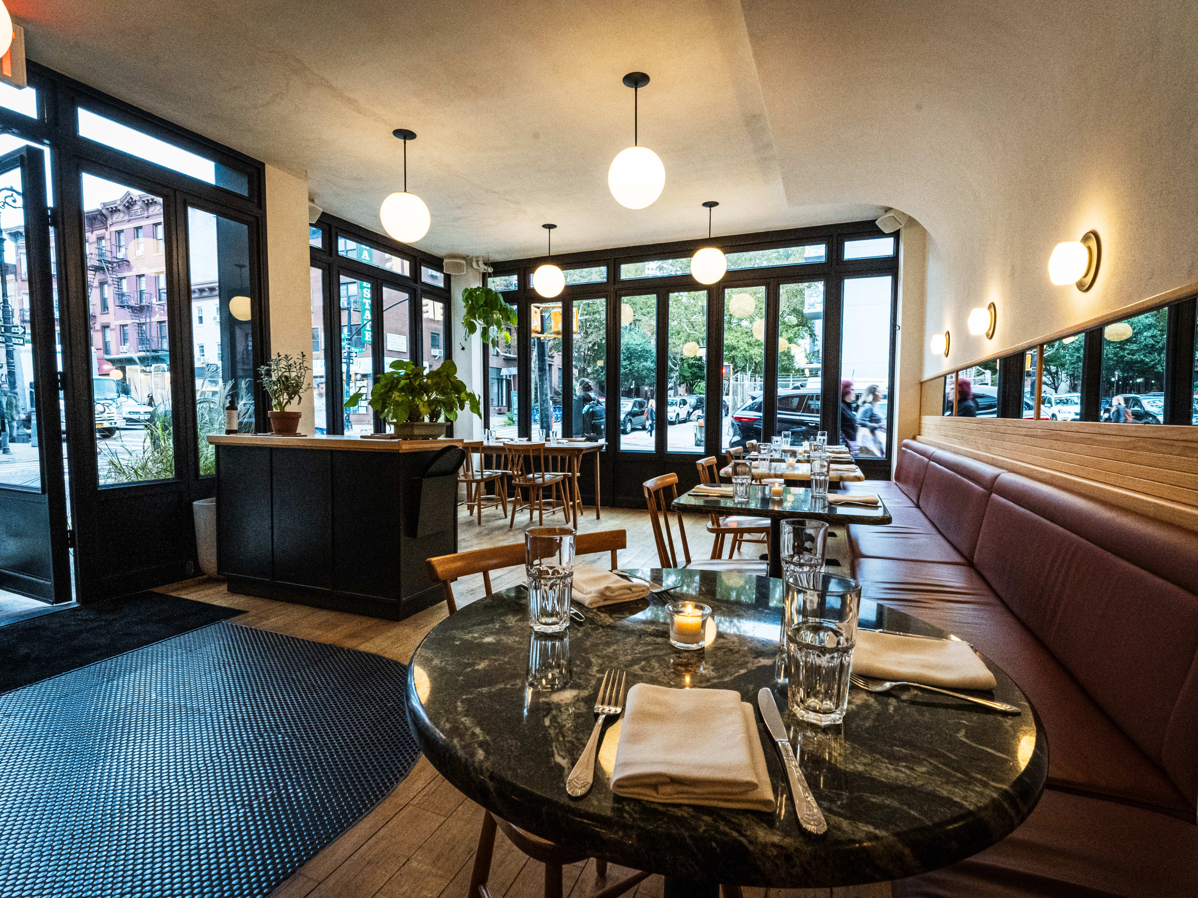 A small restaurant with big windows, globe lights, and maroon banquettes.