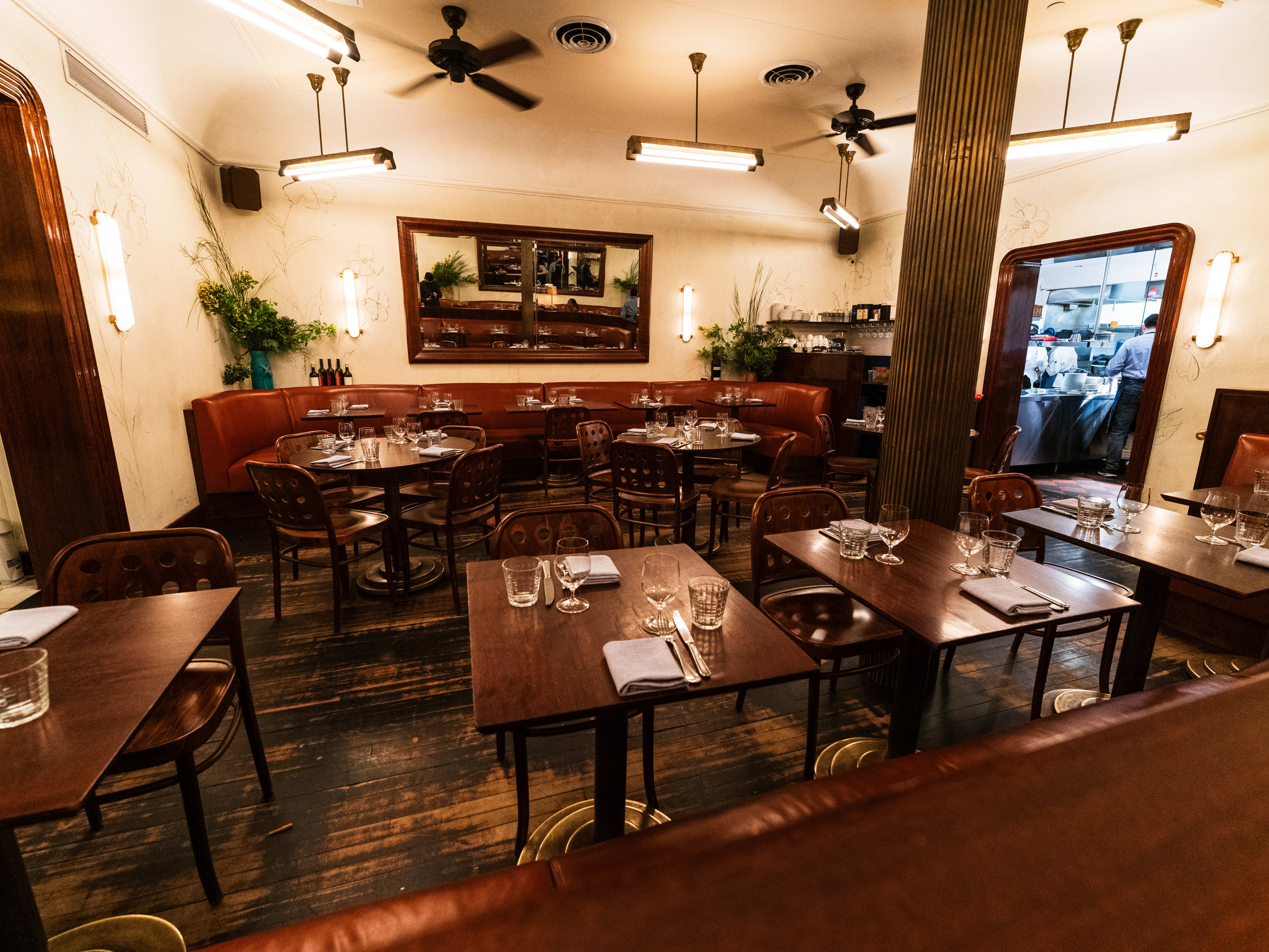 The interior of a small French restaurant with dark wooden tables and maroon banquettes.