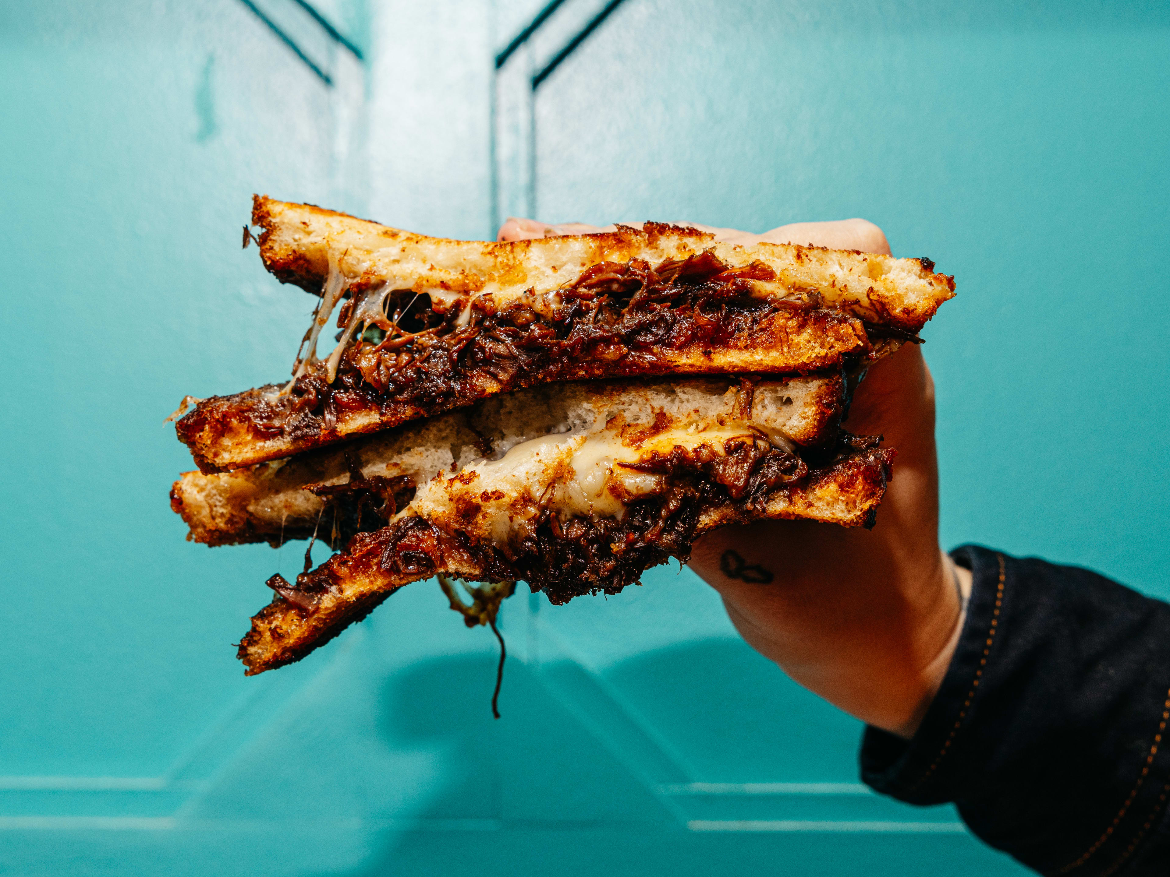 A hand holding an oxtail grilled cheese sandwich.