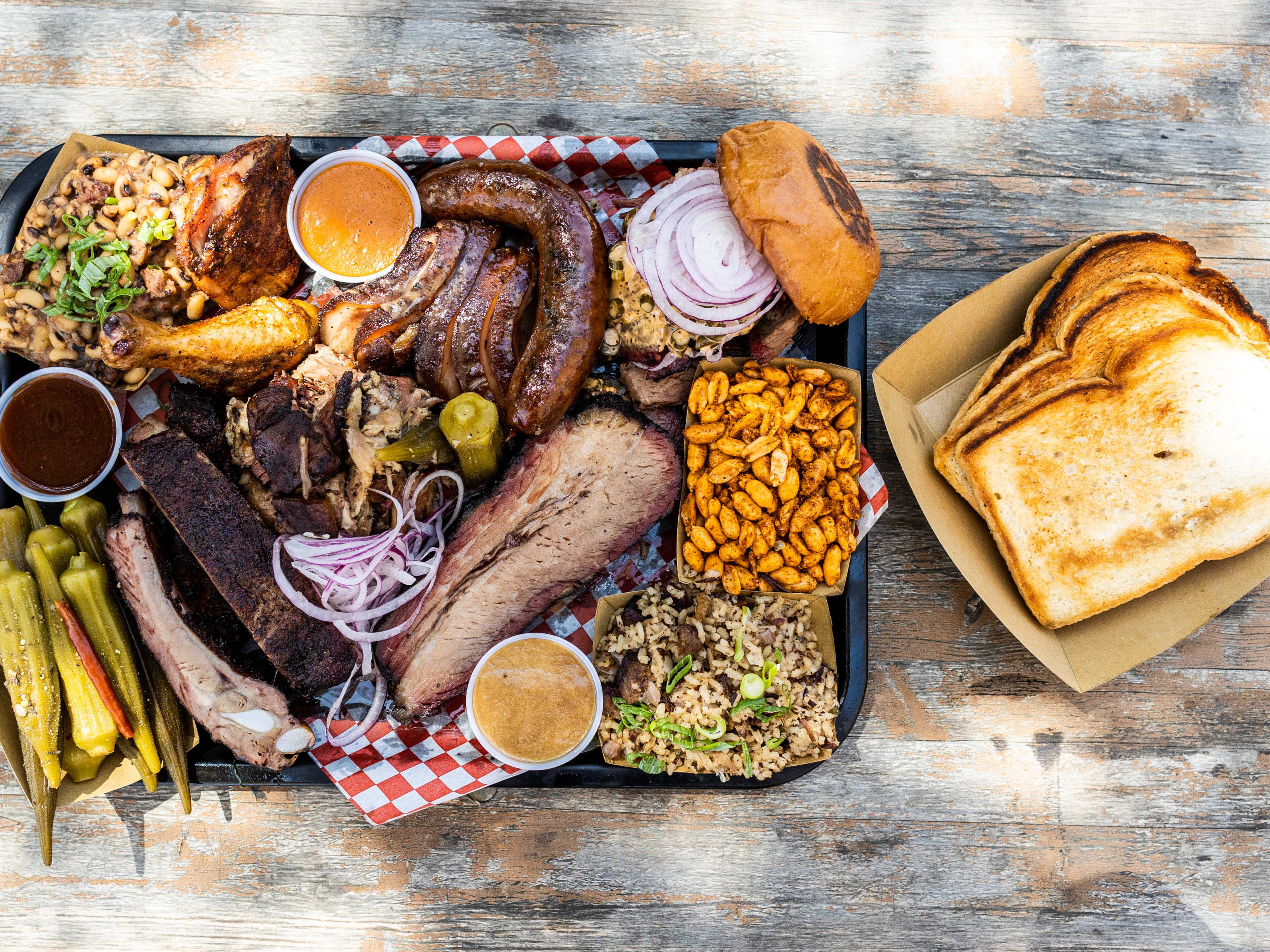 A spread of barbecued meats and sides on a tray with a side of bread.