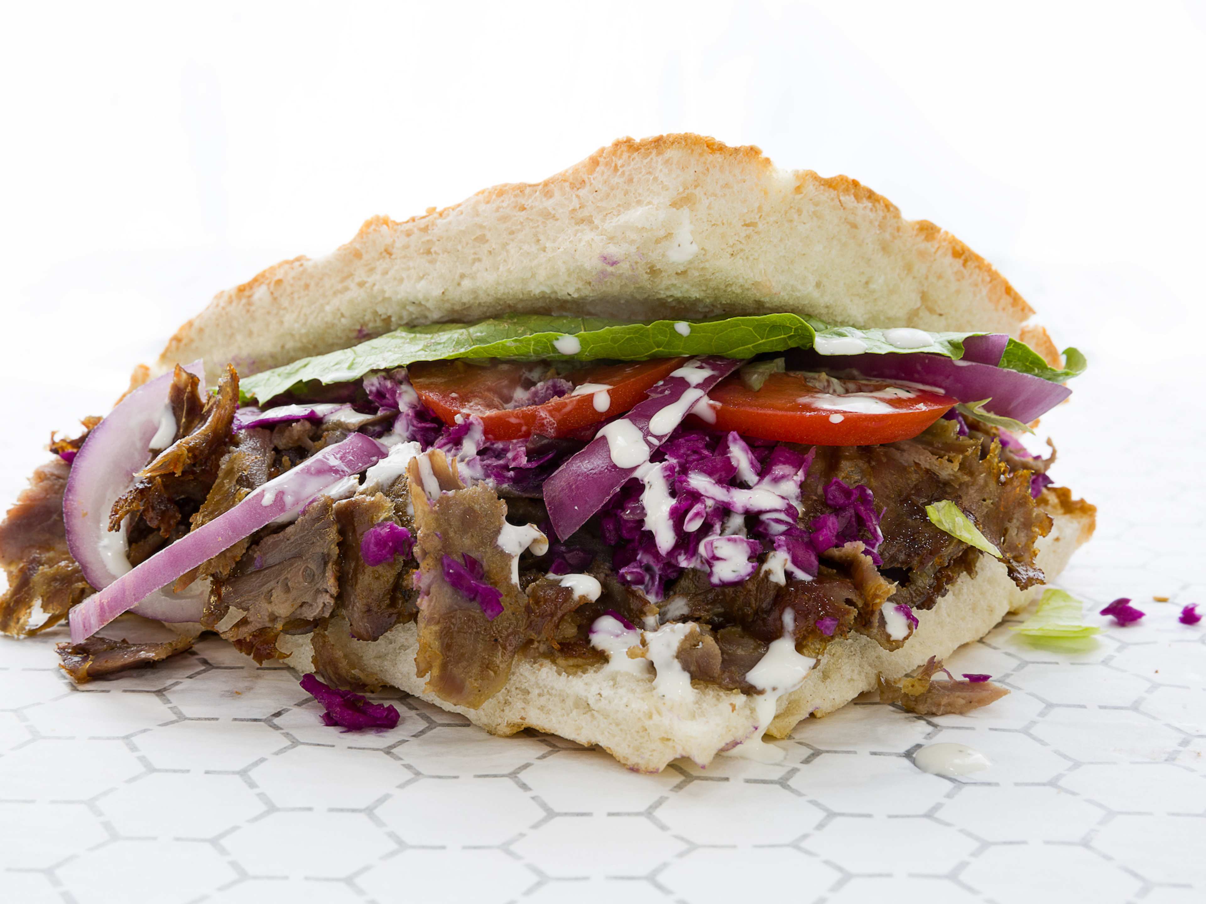 A döner kebab sandwich with beef, vegetables, and garlic sauce.