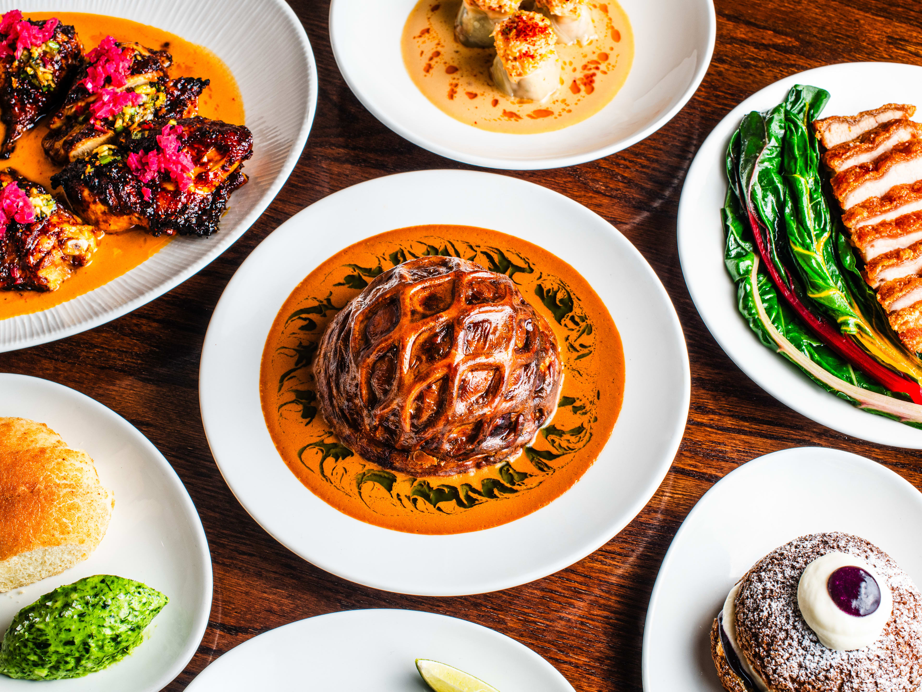 A lamb shoulder pie surrounded by other various dishes from Donia all served on white plates.