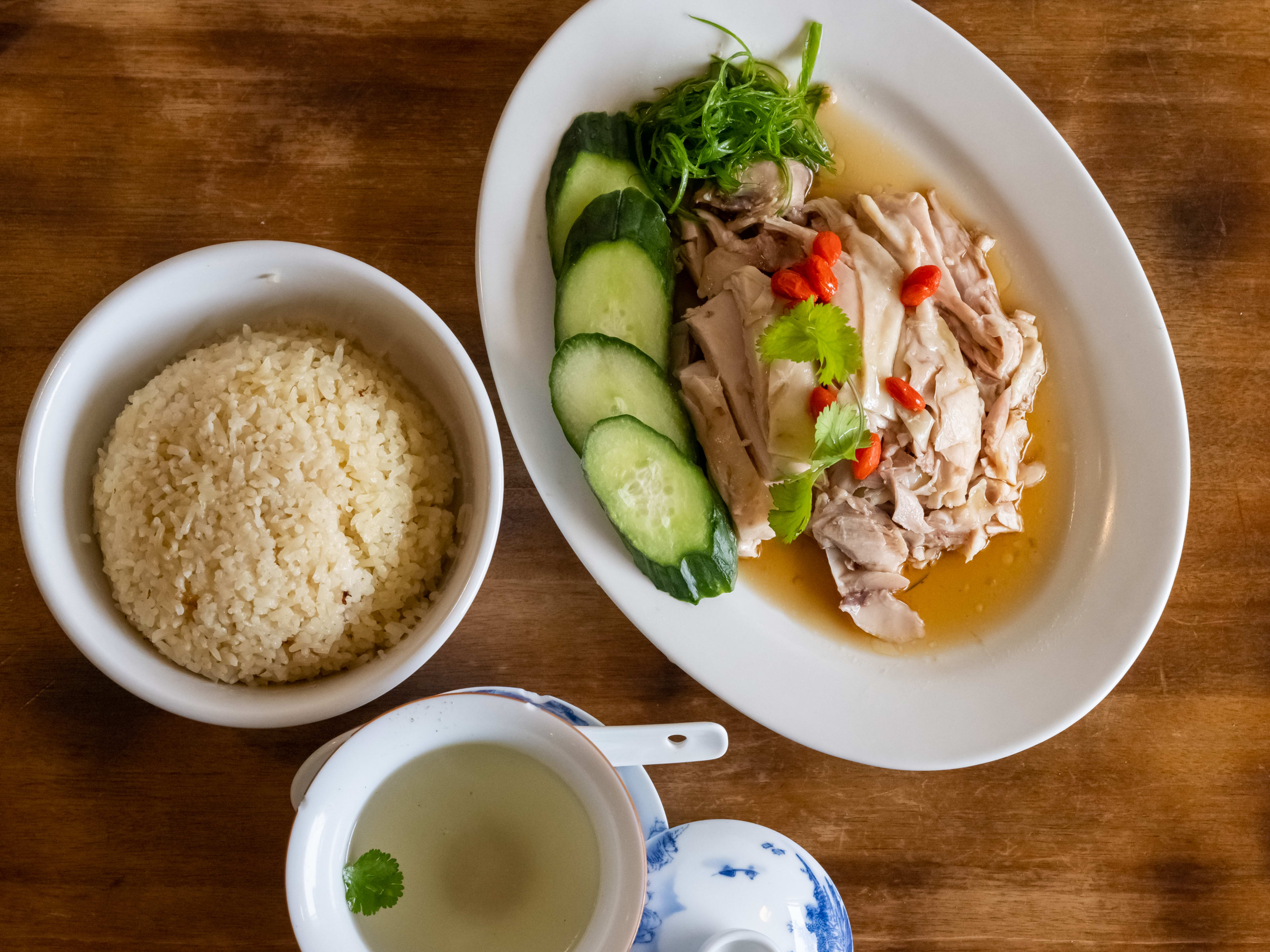 Plate of hainanese chicken rice with a cup of broth on the side