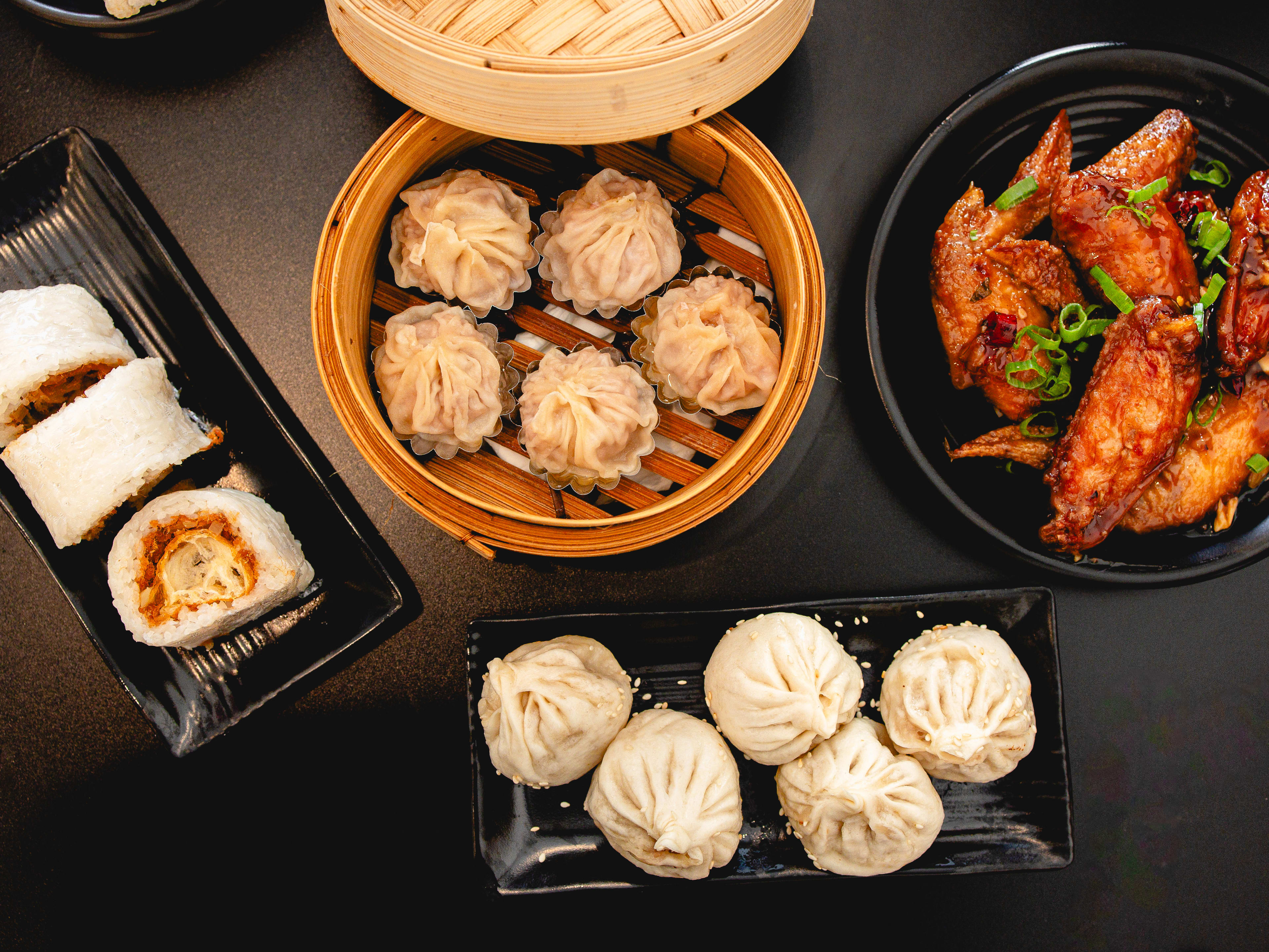 A group shot of xiao long bao, sticky rice roll, chicken wings, and pan-fried pork buns at Dumpling Specialist