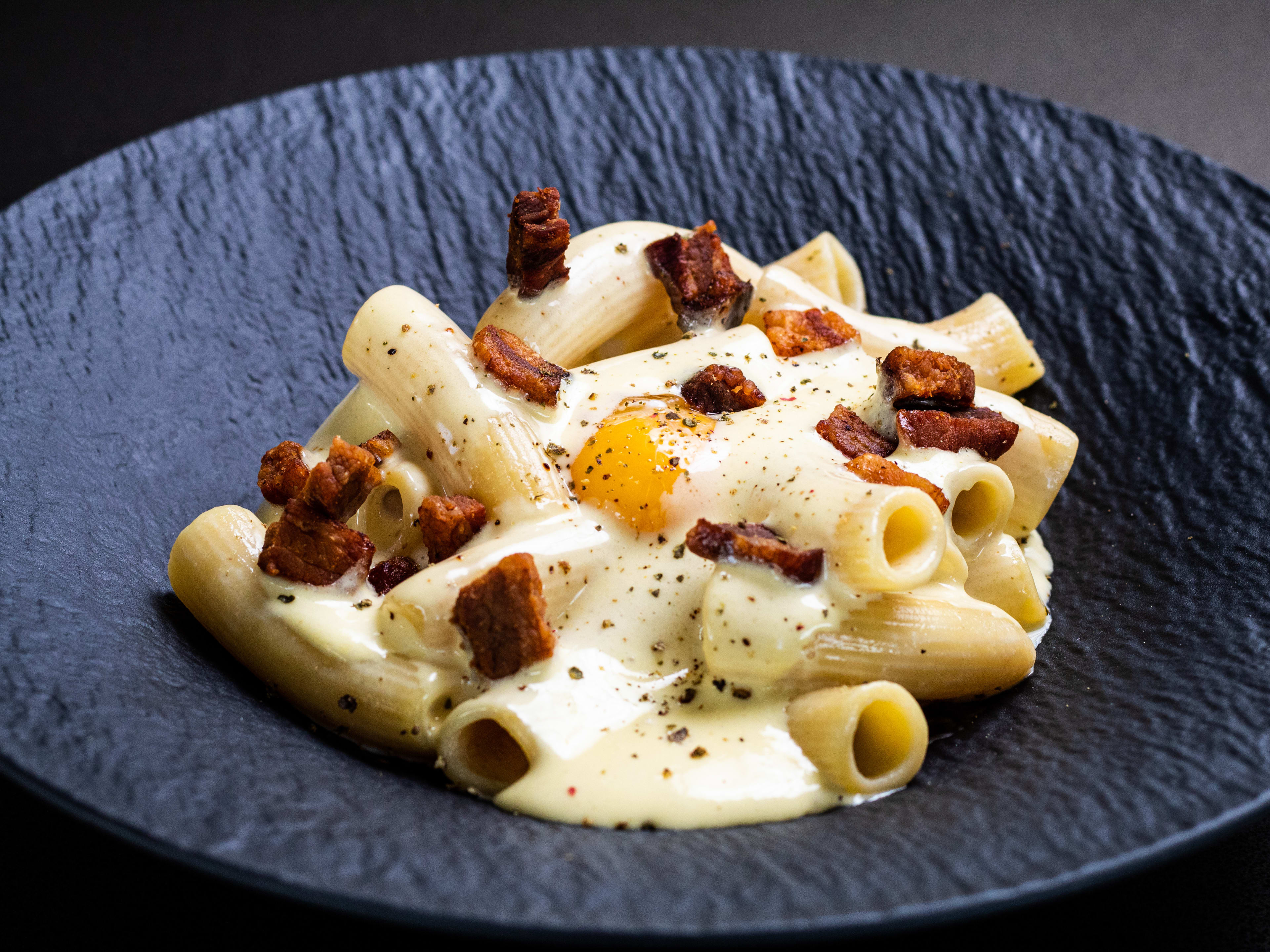 A black bowl of rigatoni carbonara.