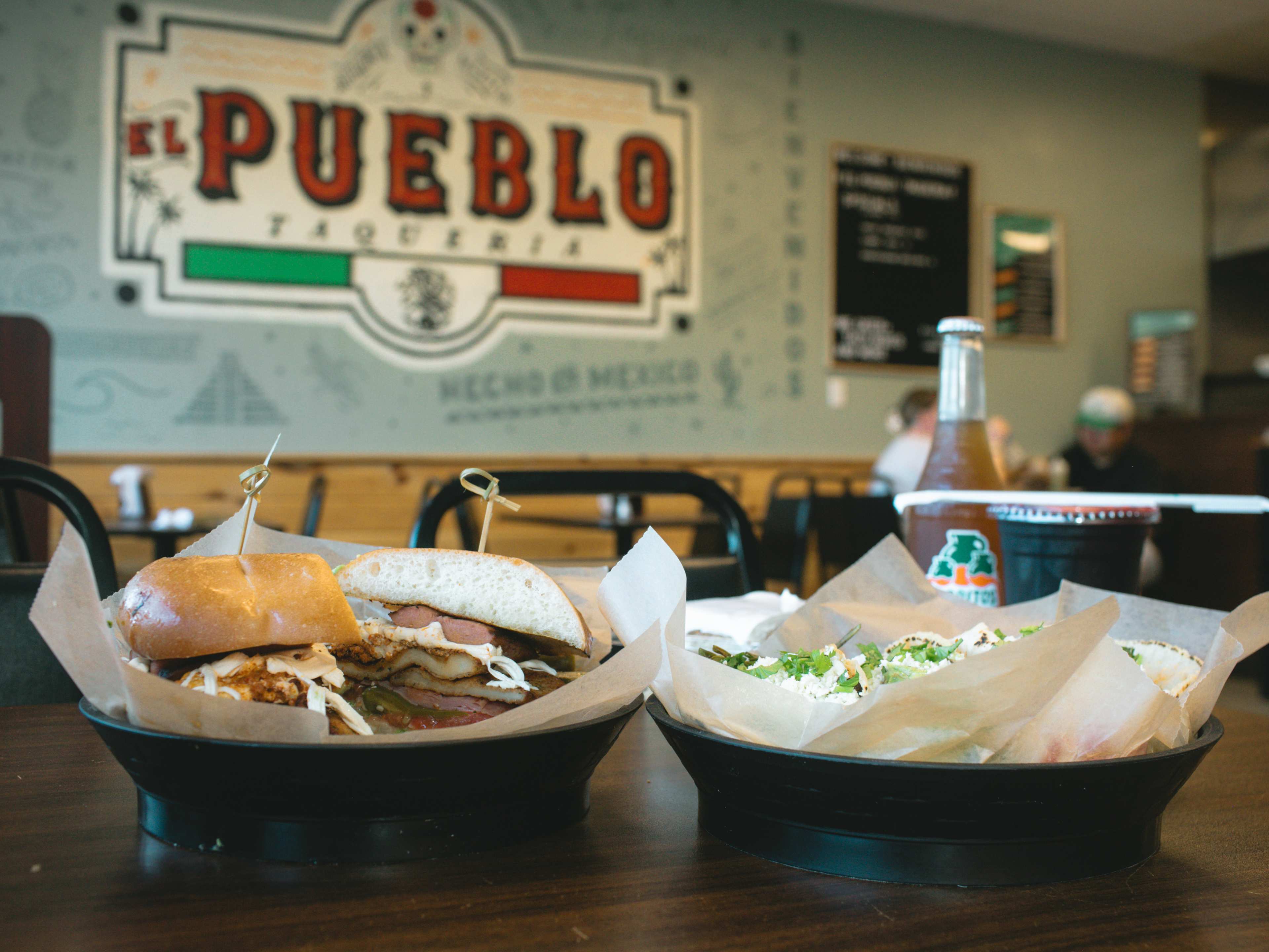 A torta and tacos on a table in front of a sign that says El Pueblo Taqueria