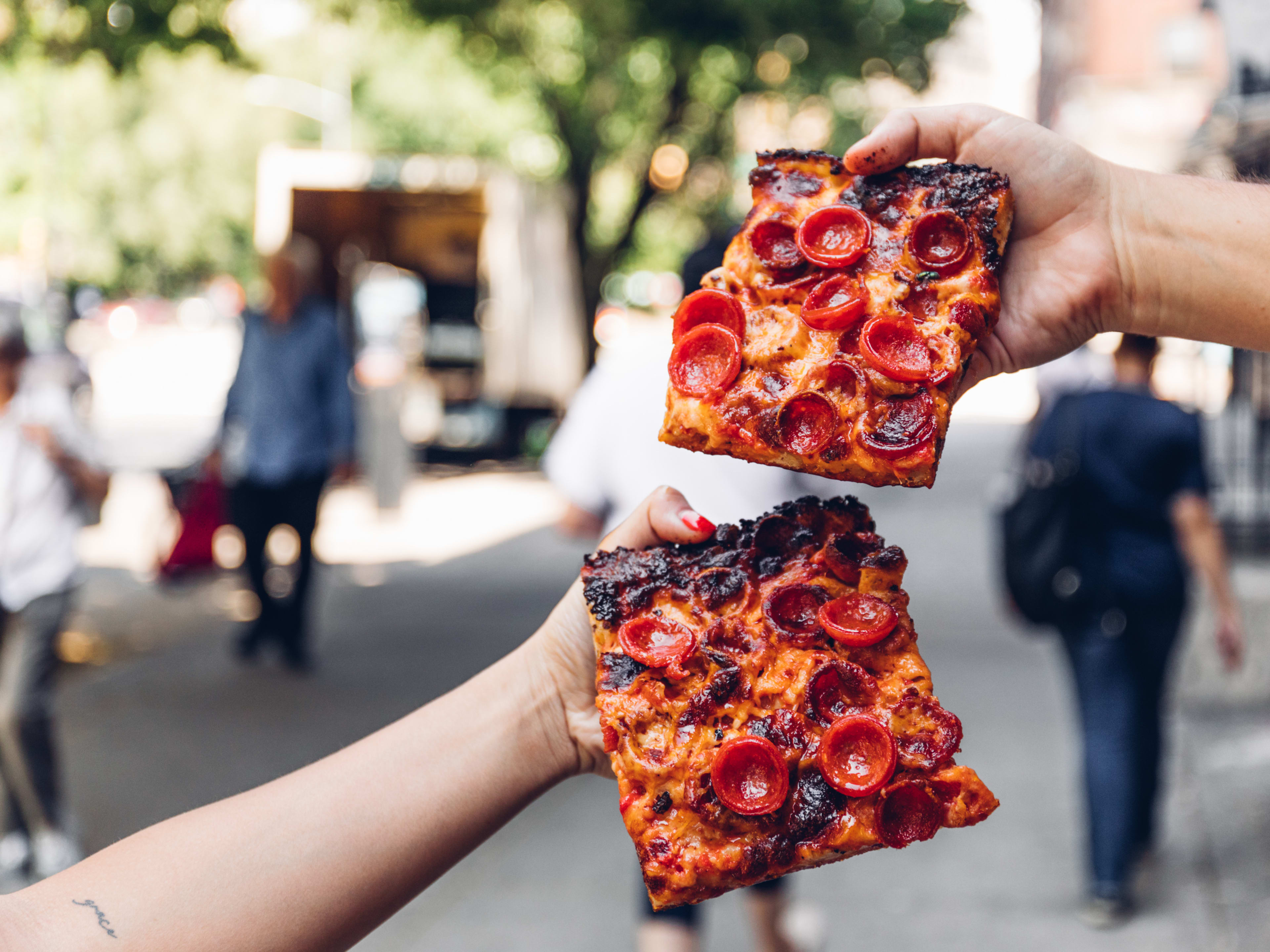 People hold up two slices of pizza from Mama's Too.