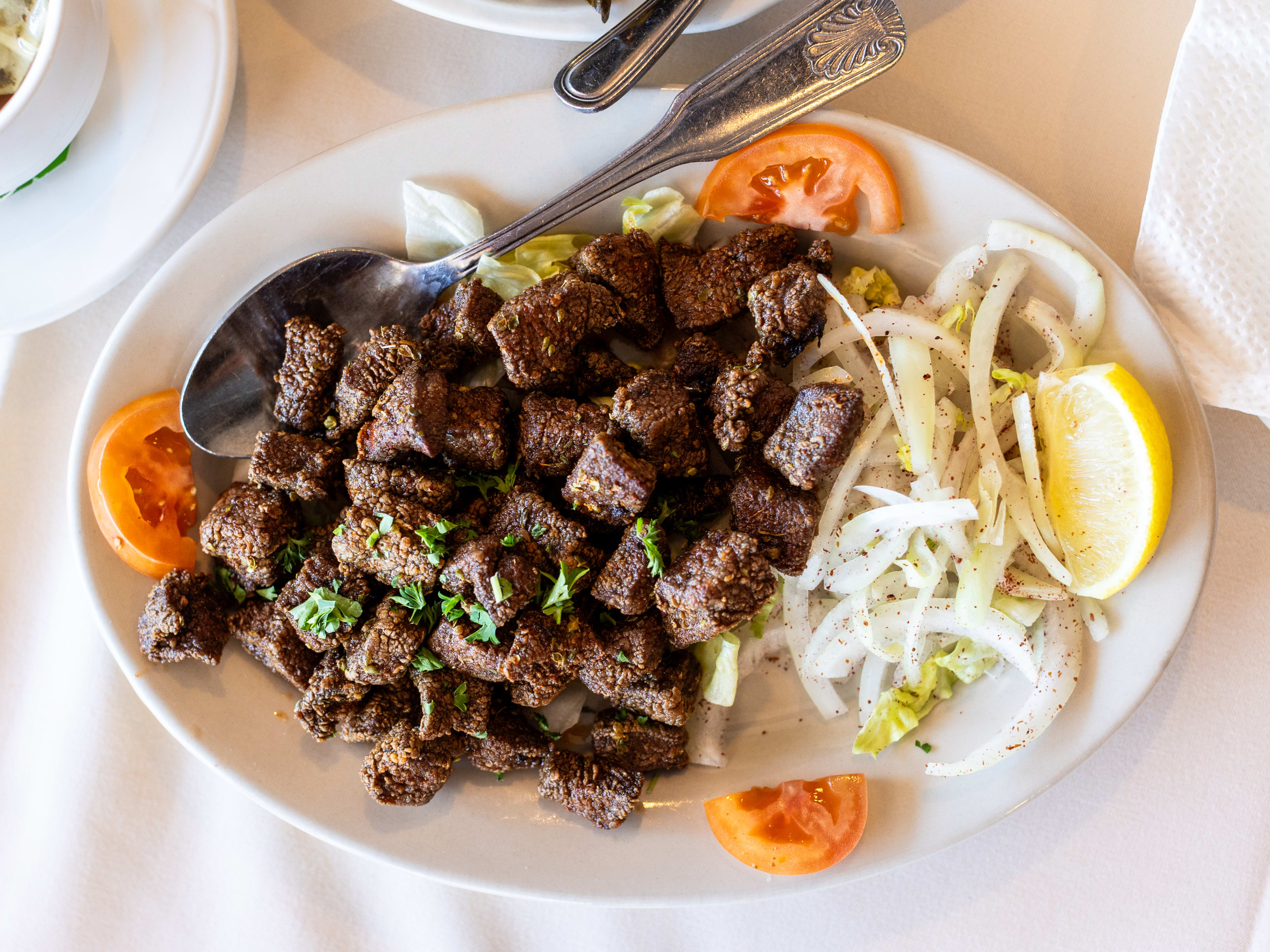 Fried liver and a side of onions, tomatoes and a lemon wedge on a white plate.