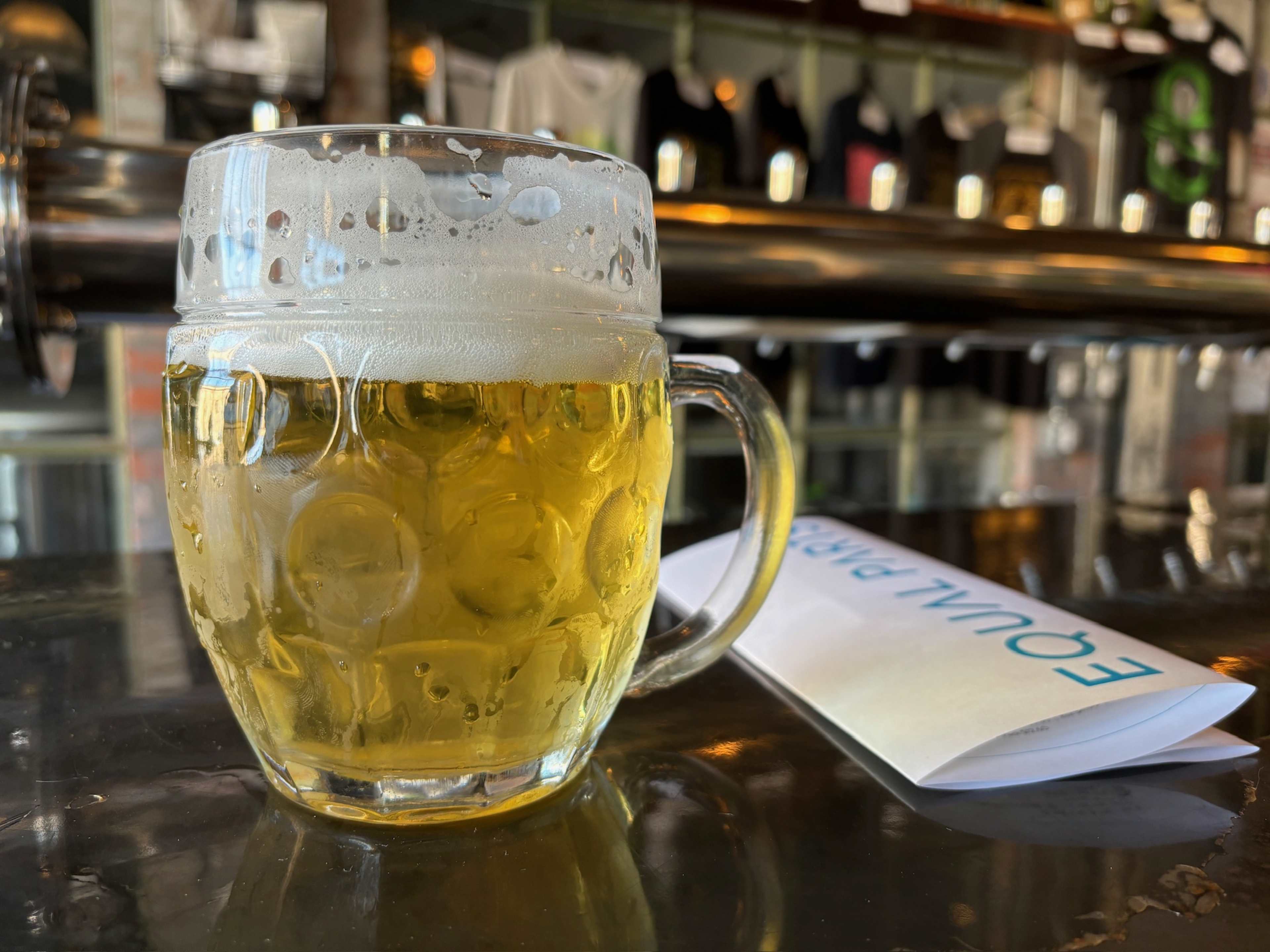 large foamy pint of light pilsner beer next to a menu for Equal Parts Brewery