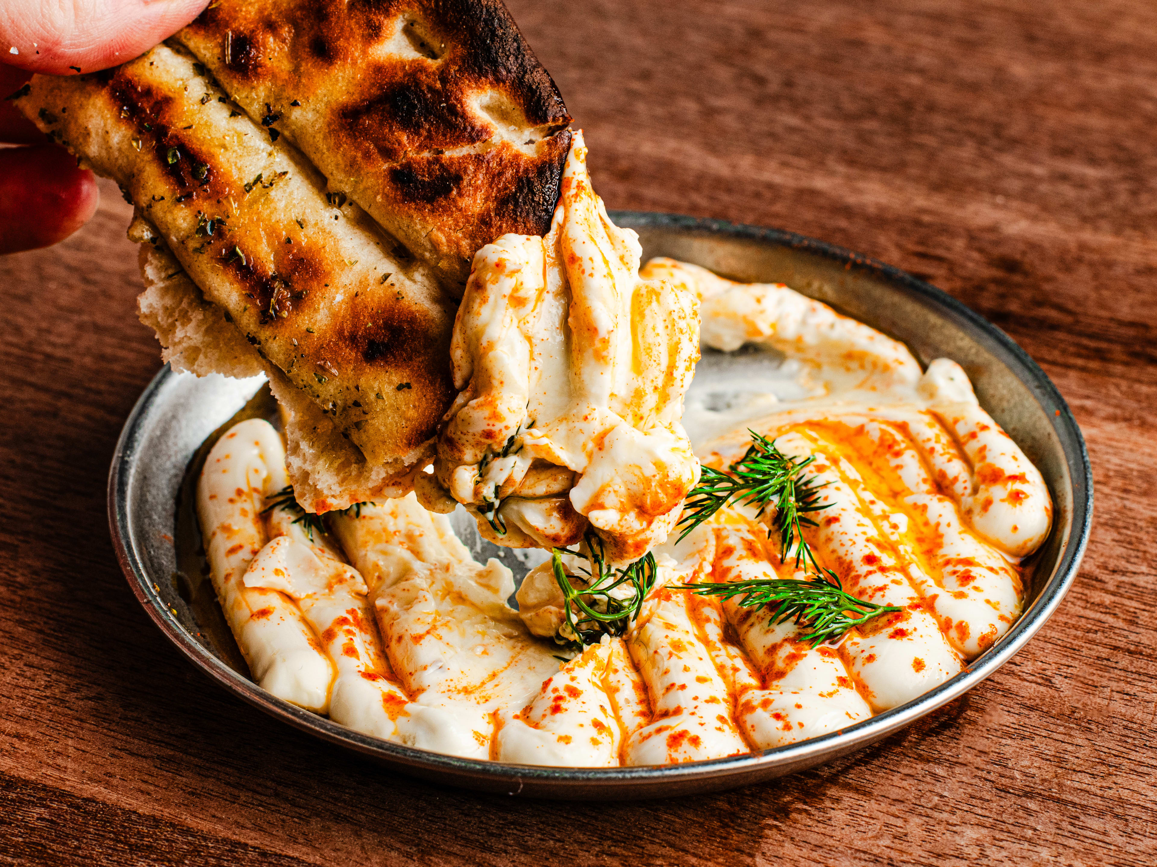 A person dips the grilled flatbread into a metal bowl of Taramasalata from Evi's.