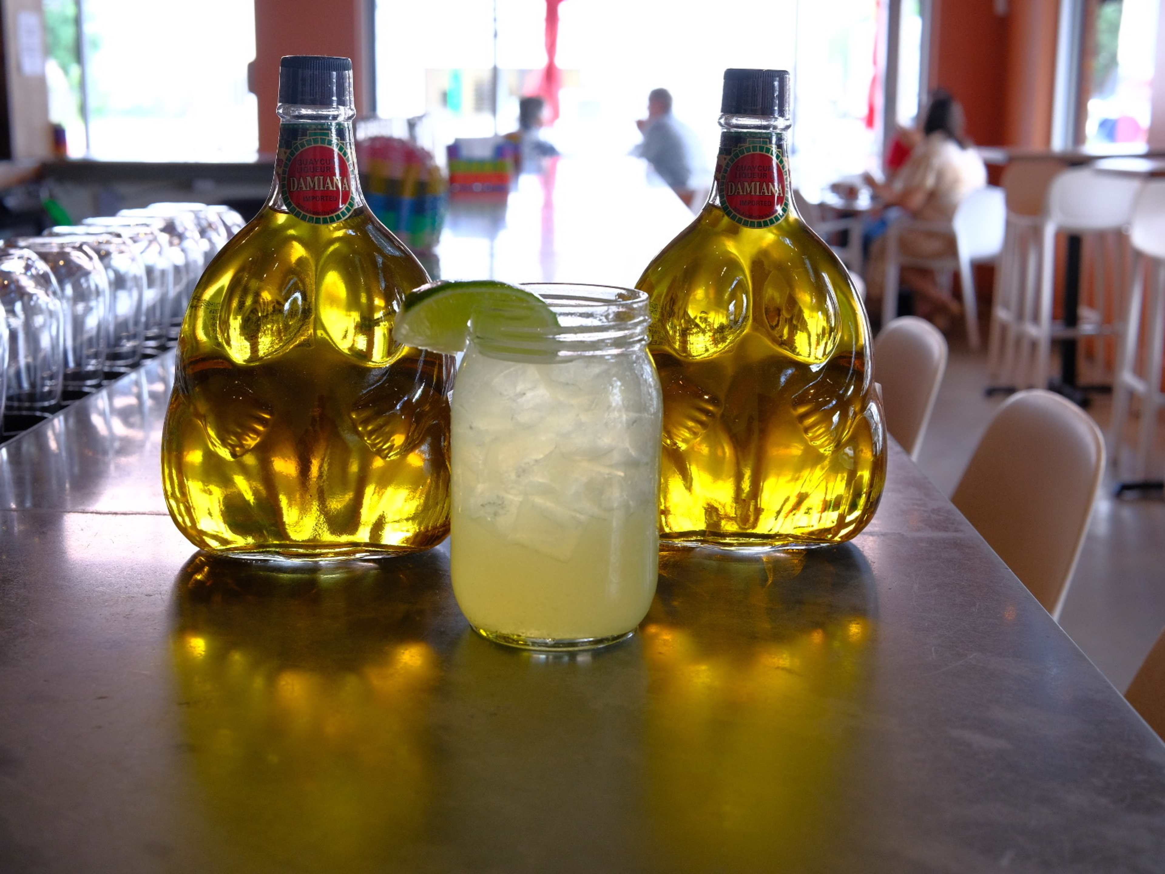 margarita in a mason jar surround by two large bulbous bottles filled with golden yellow liquid