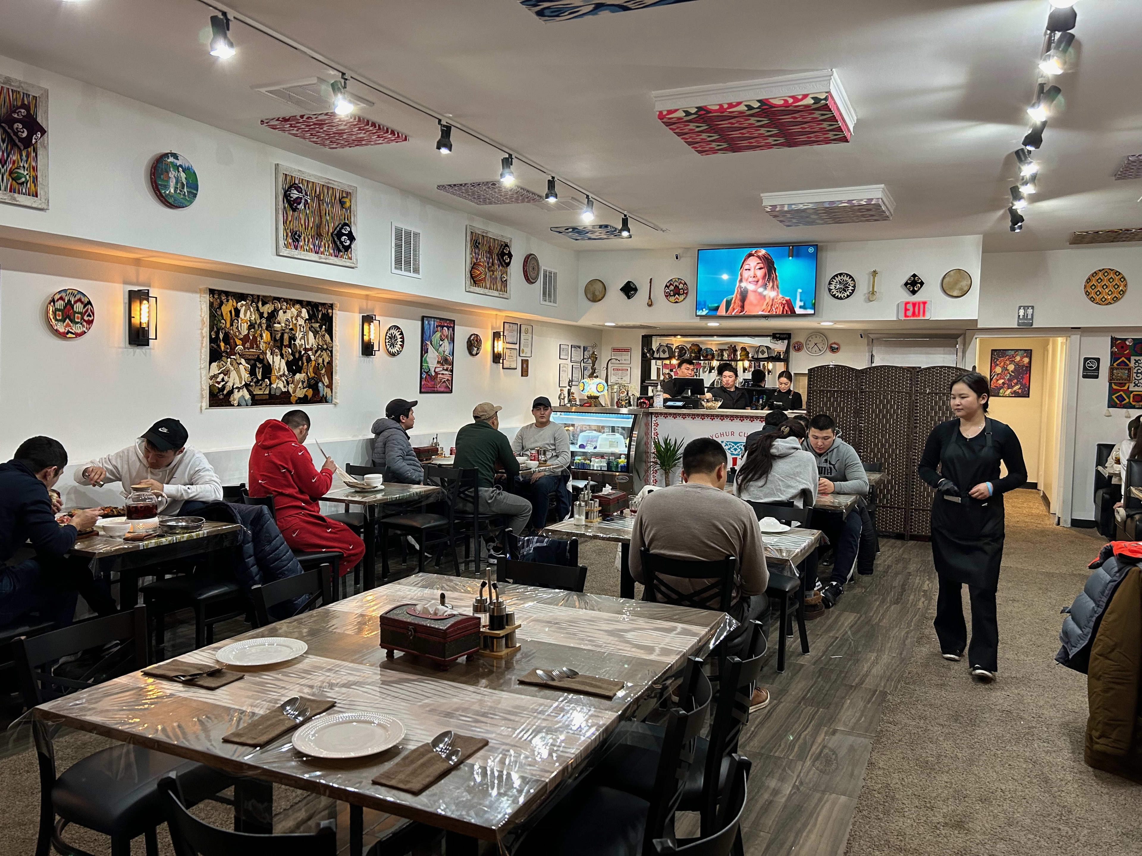 A bright dining room with tables full of people and decorations like tapestries, paintings, and ceramics hanging from the walls.