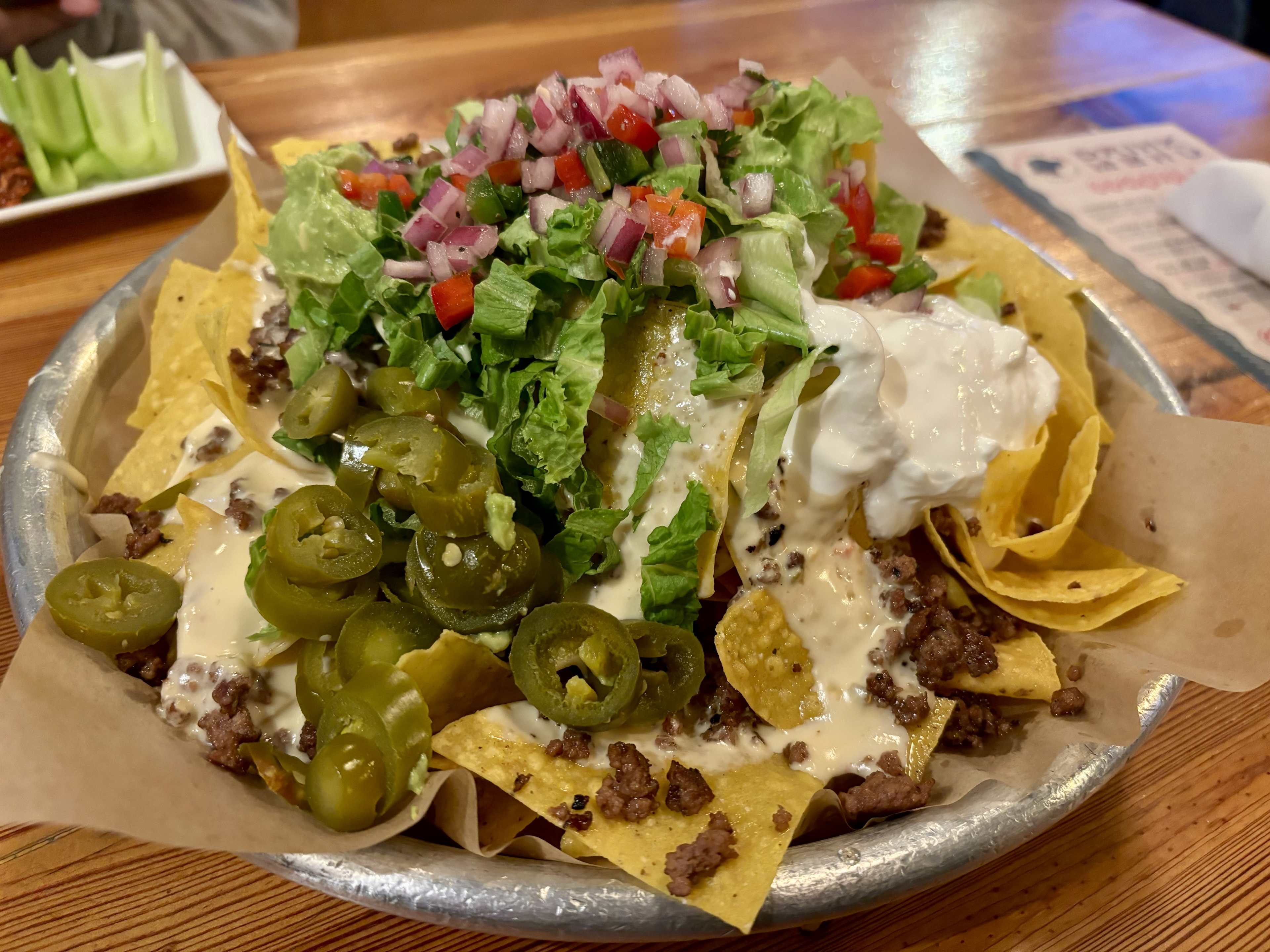 A mountain of nachos with ground beef, queso, jalapeños, onions, and lettuce.