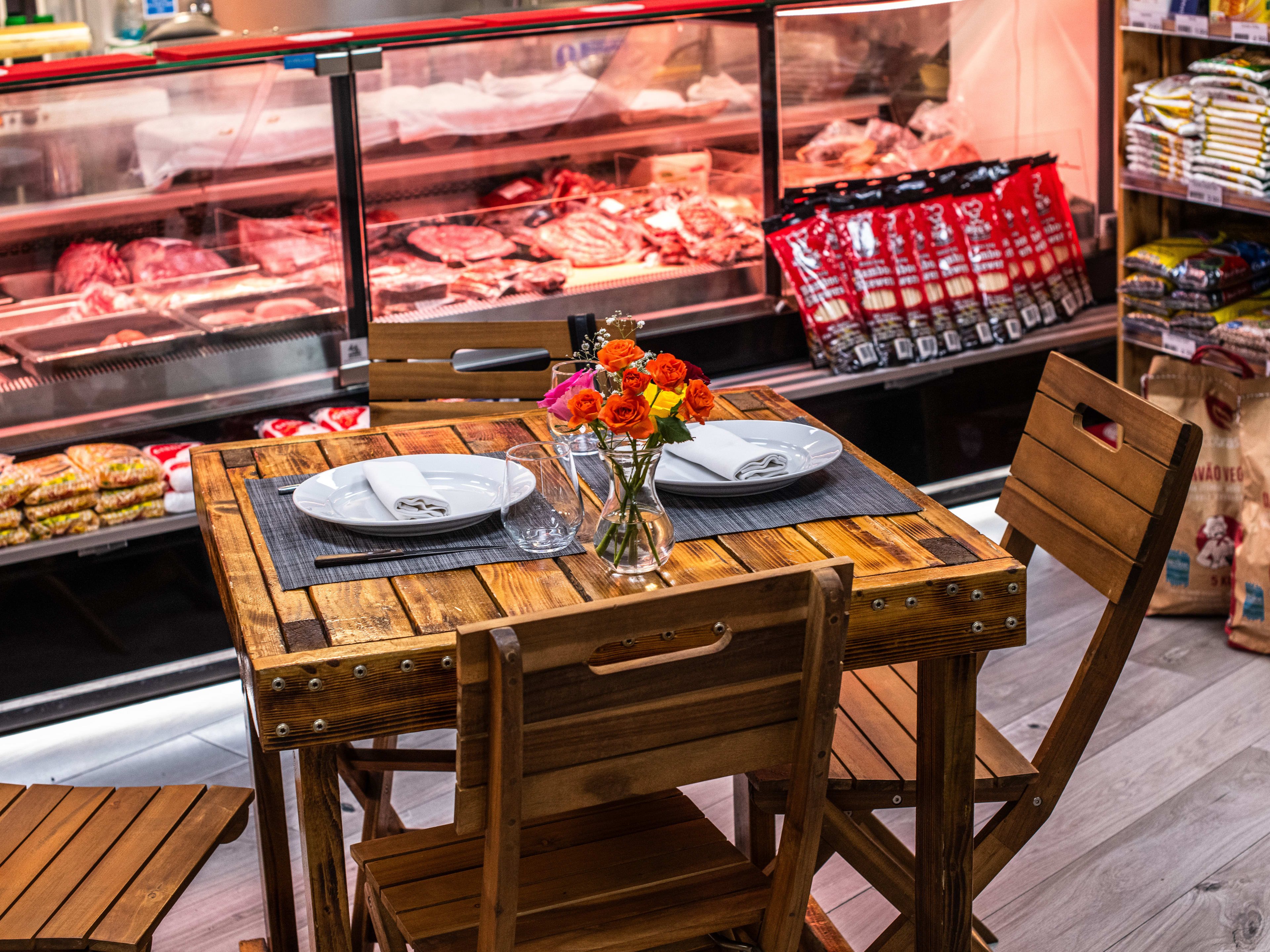 A small wooden table with a vase of flowers next to the meat case at Fine Cut Butchers.