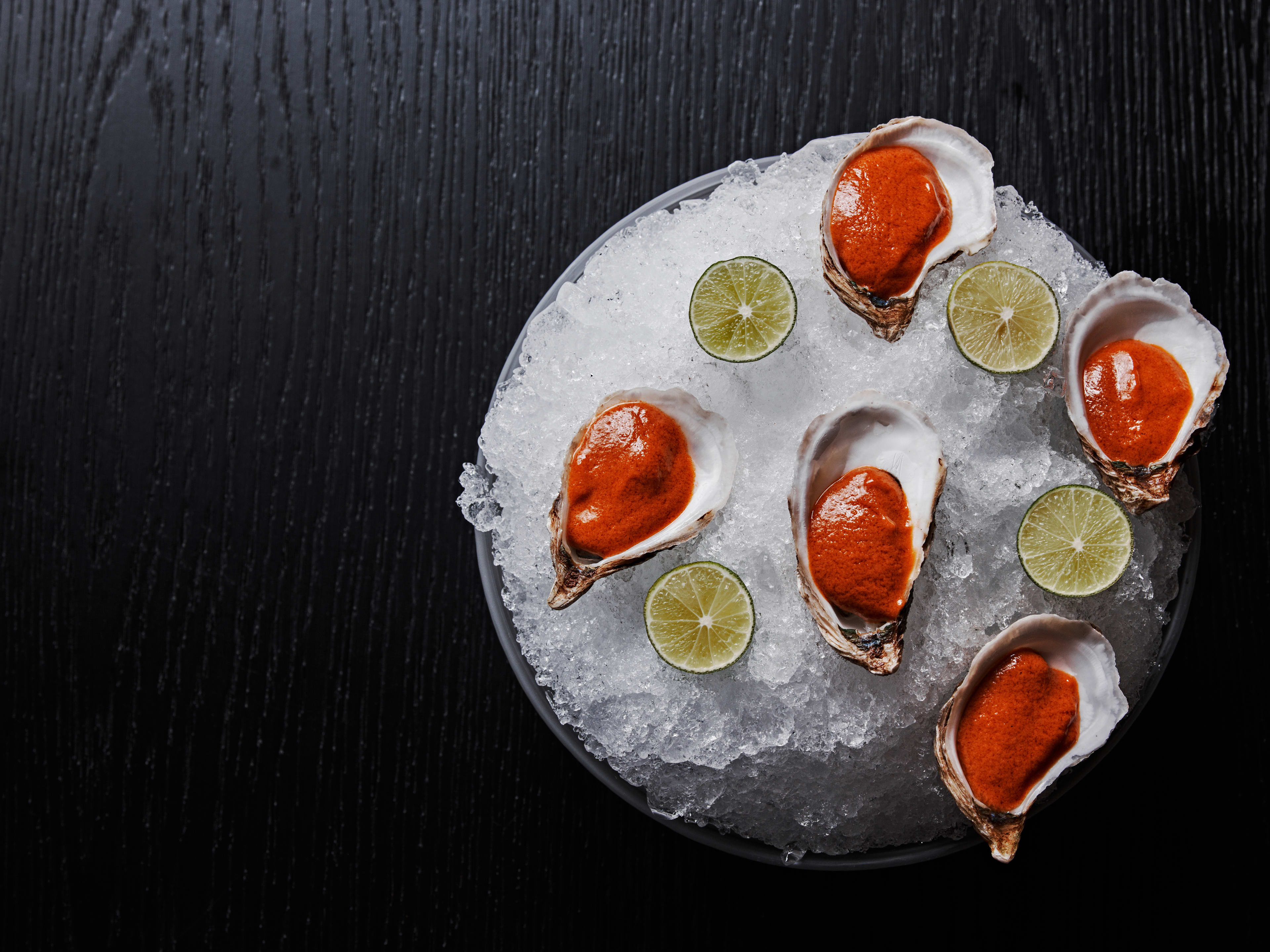 Five raw oysters arranged over ice with a thick red sauce over each.