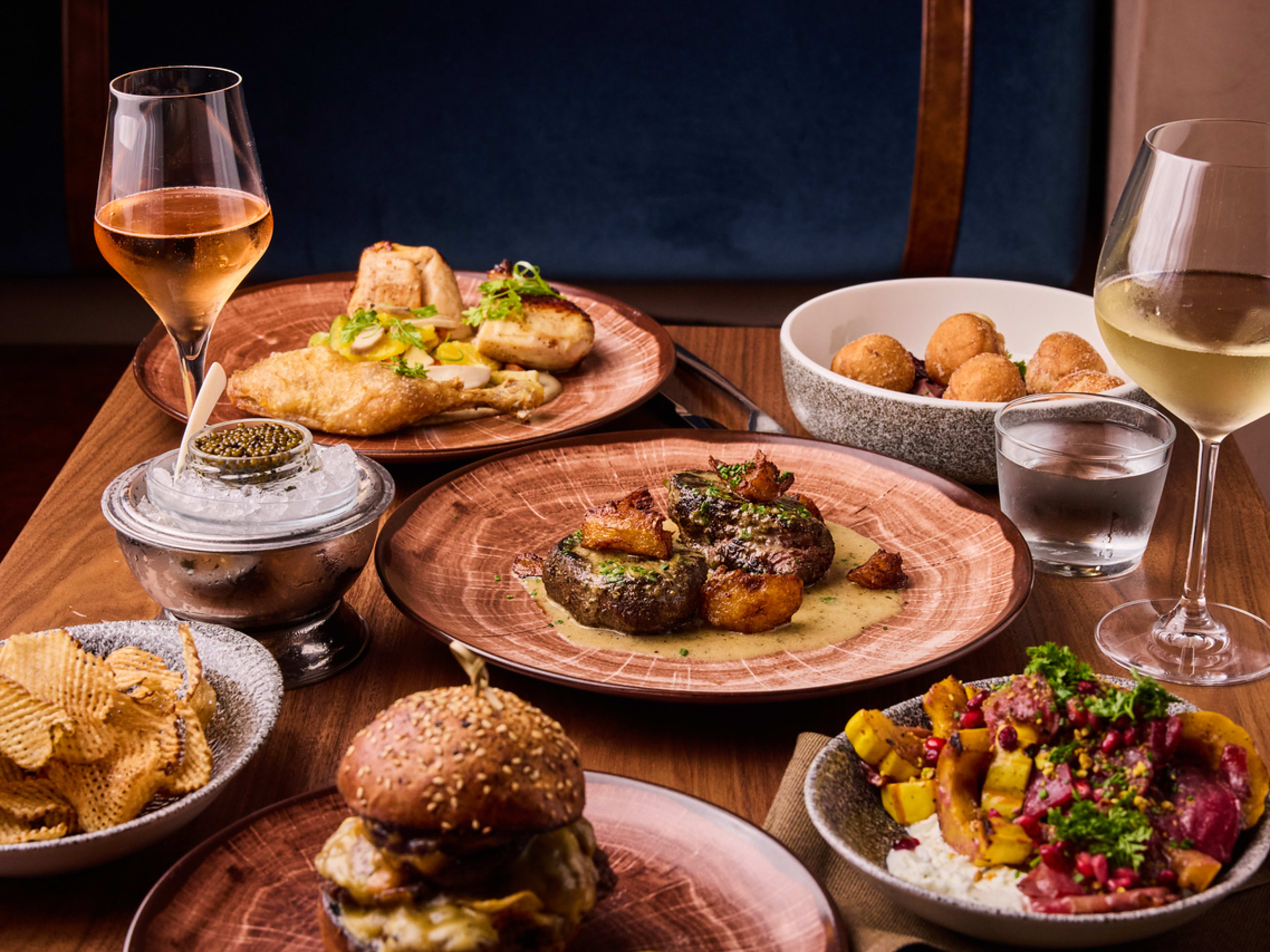 spread of small plates, steak, cheeseburger, caviar, and glasses of wine