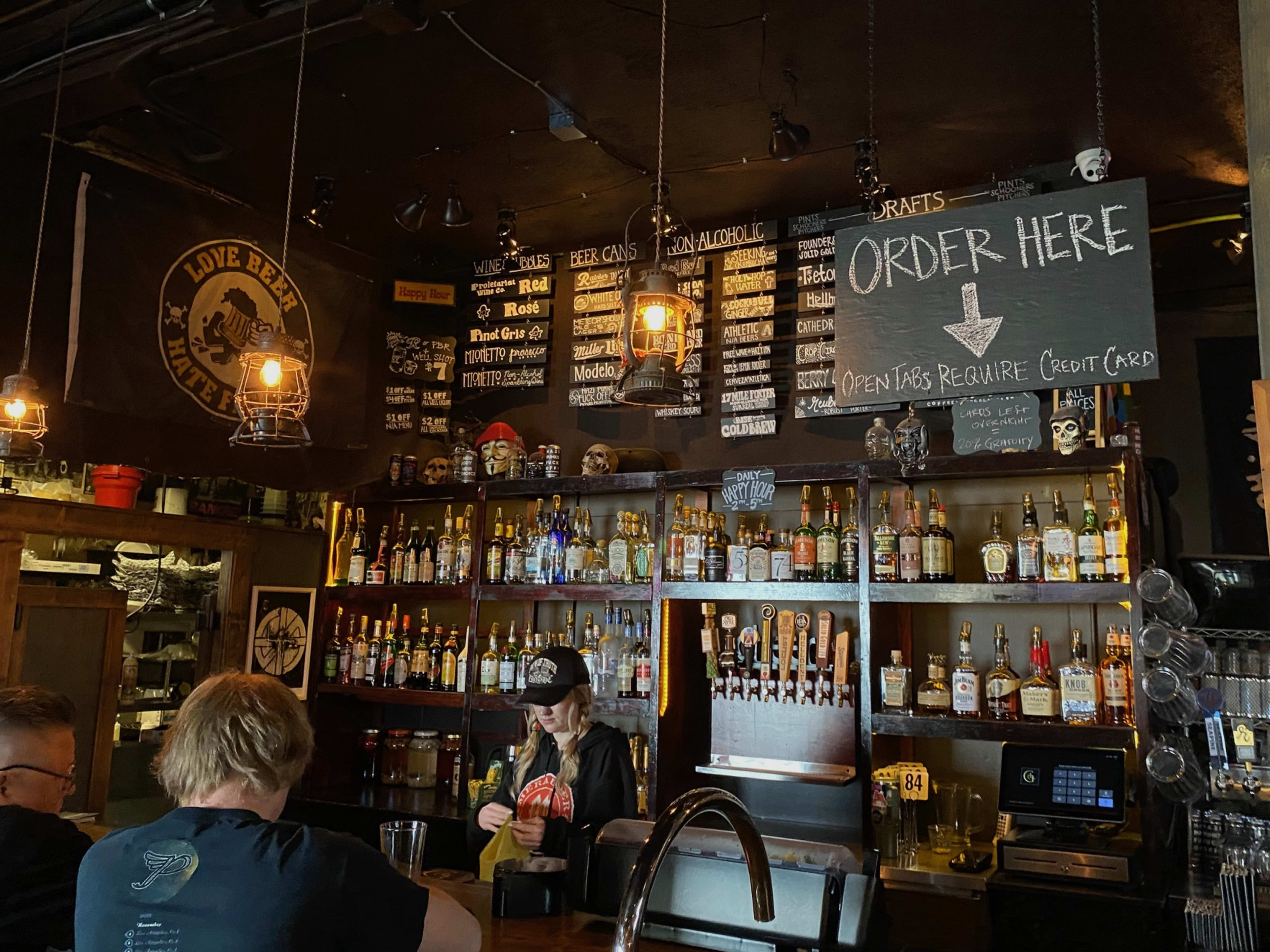 The back of a bar with a bunch of liquor bottles and handwritten chalk signs