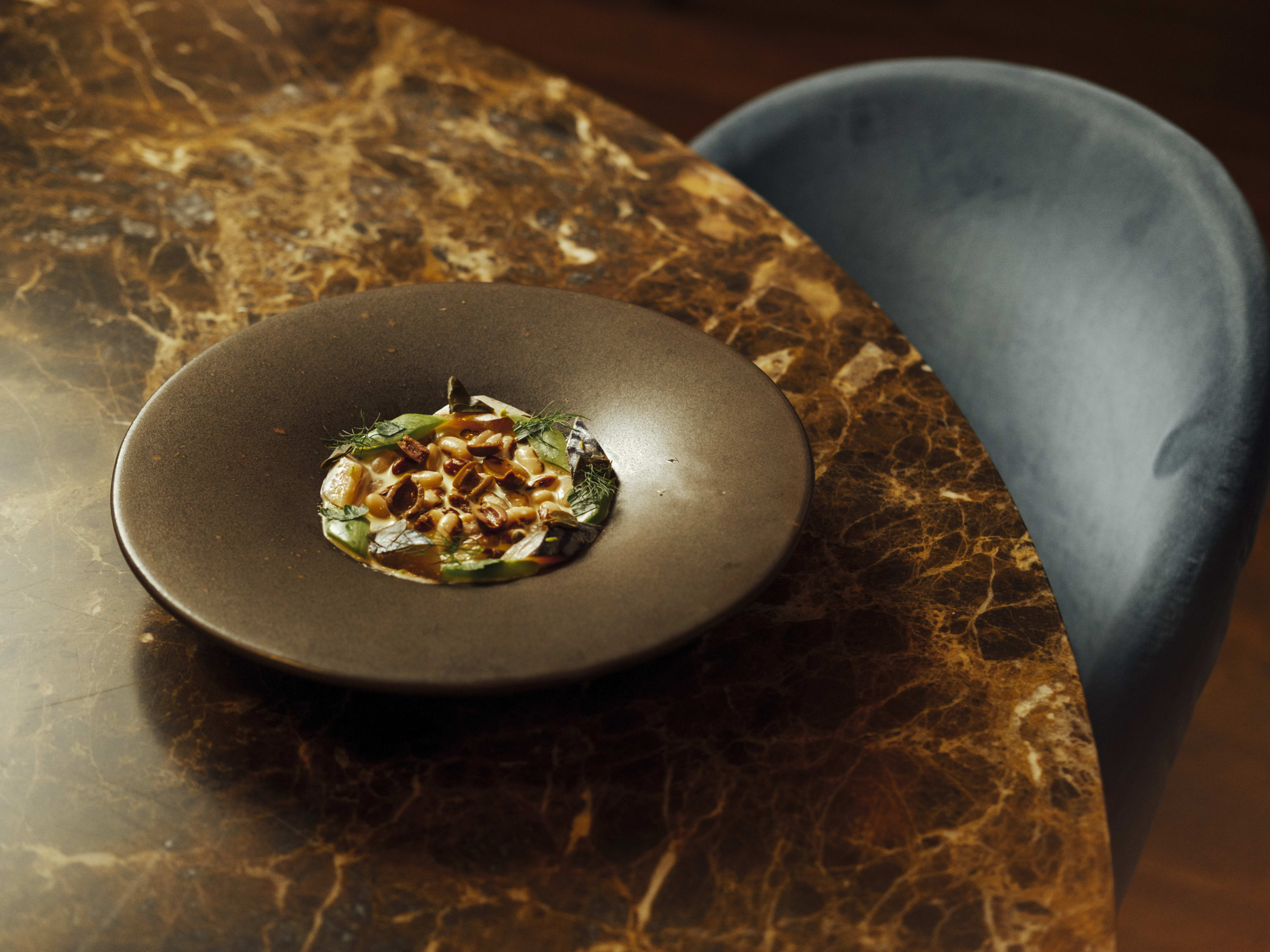 A bowl of pasta on a round table and velvet chair at Gagini, a restaurant in Palermo