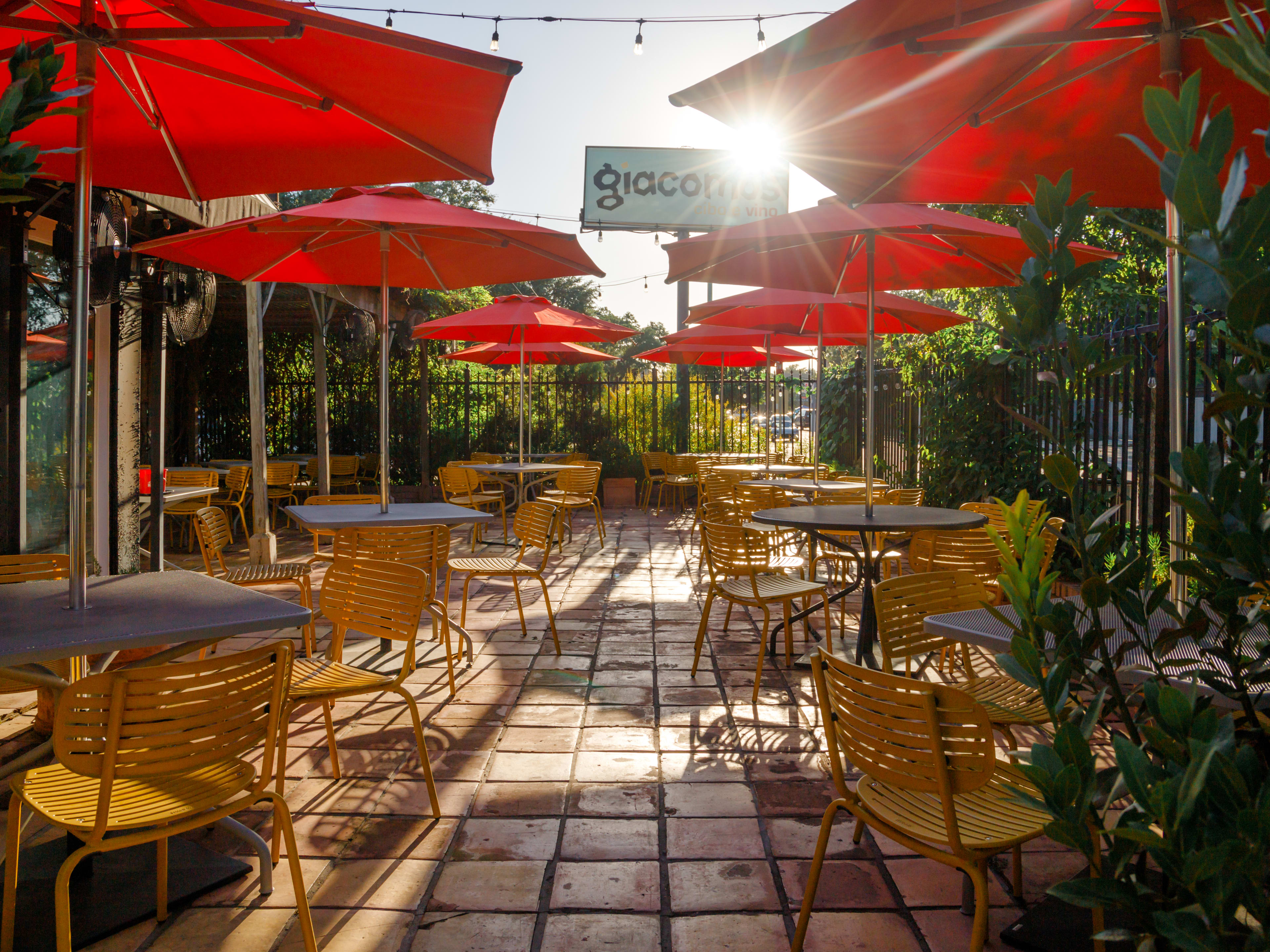 The sunlit patio of Giacomo’s Cibo E Vino with square tables with red umbrellas and yellow chairs.