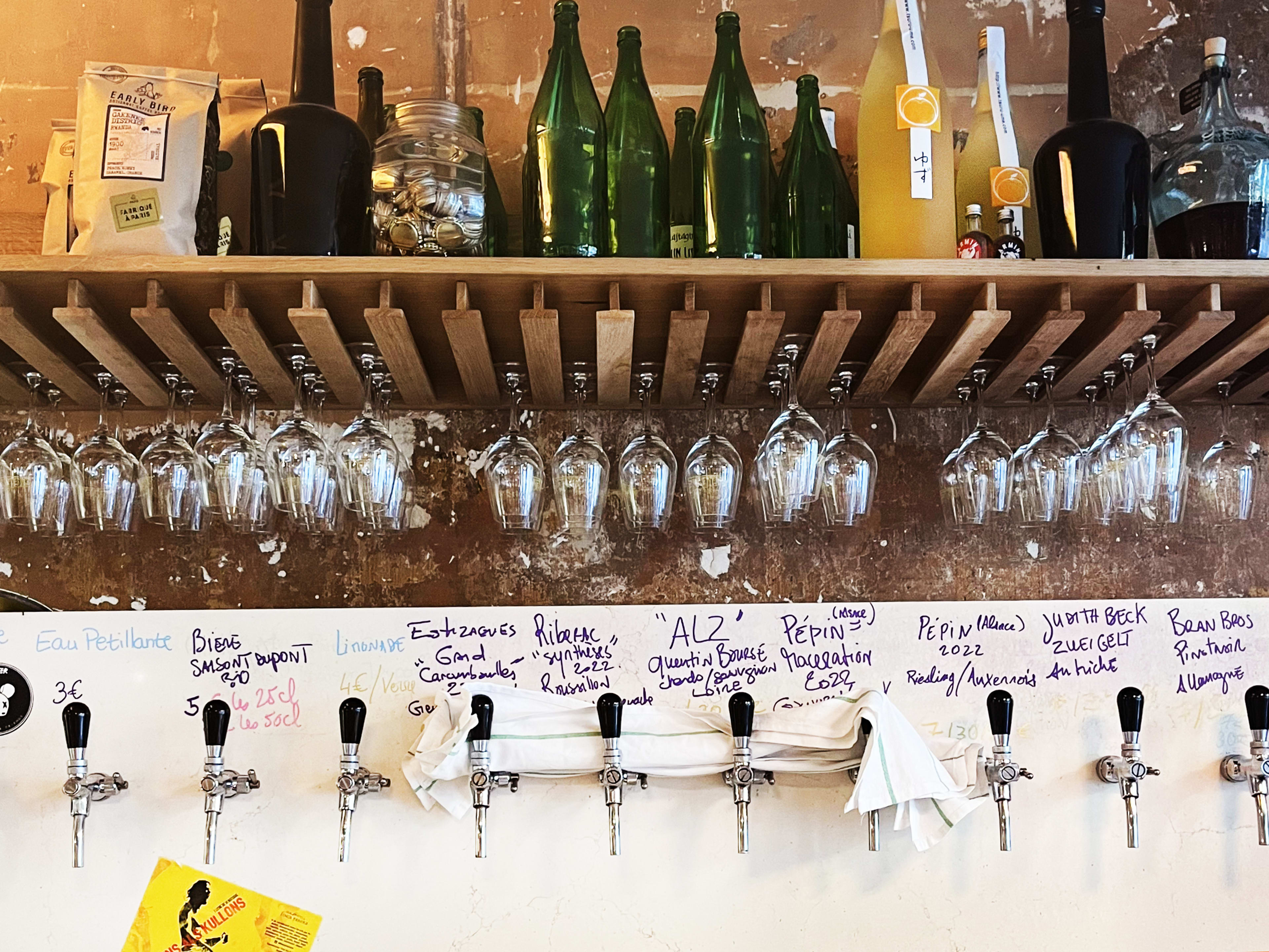 A wall of wine bottles, wine glasses, and wines on tap at Giclette, a wine bar in Paris